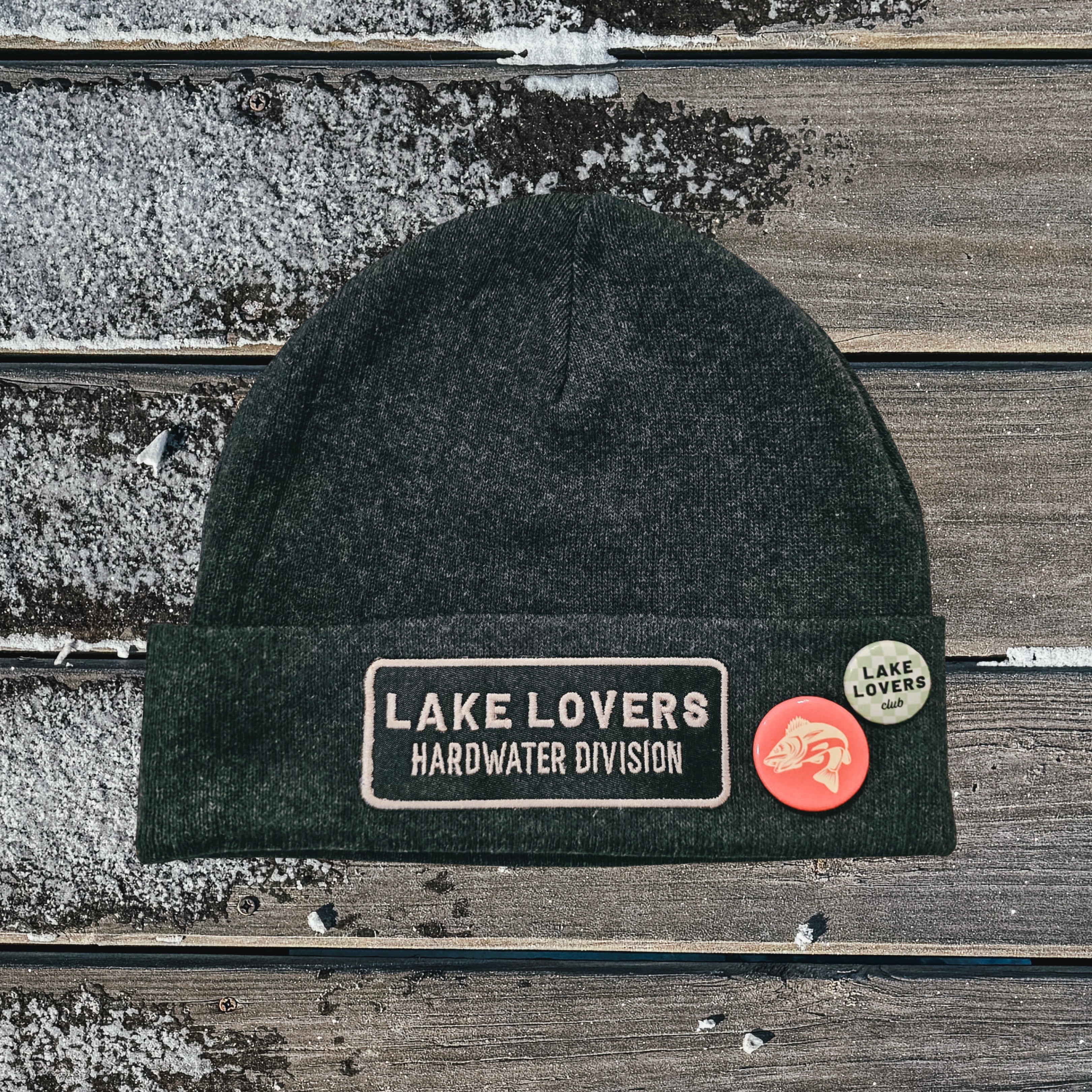Dark gray beanie with 'Lake Lovers' patches on a wooden surface