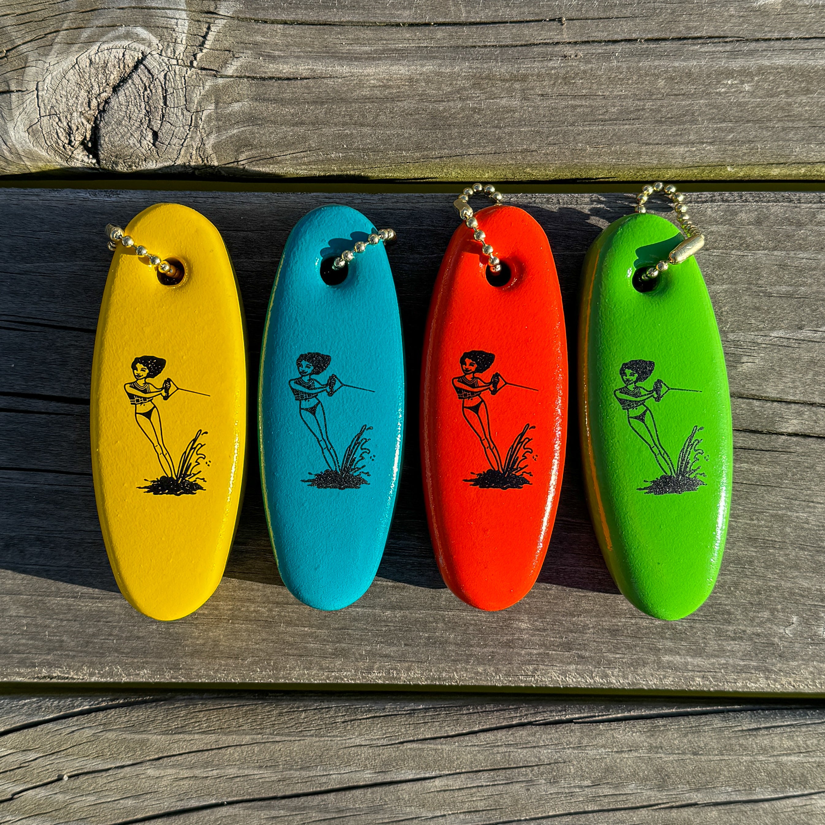 Four colorful floaty keychains with a design of a girl waterskiing on it, lying on a wooden dock surface.