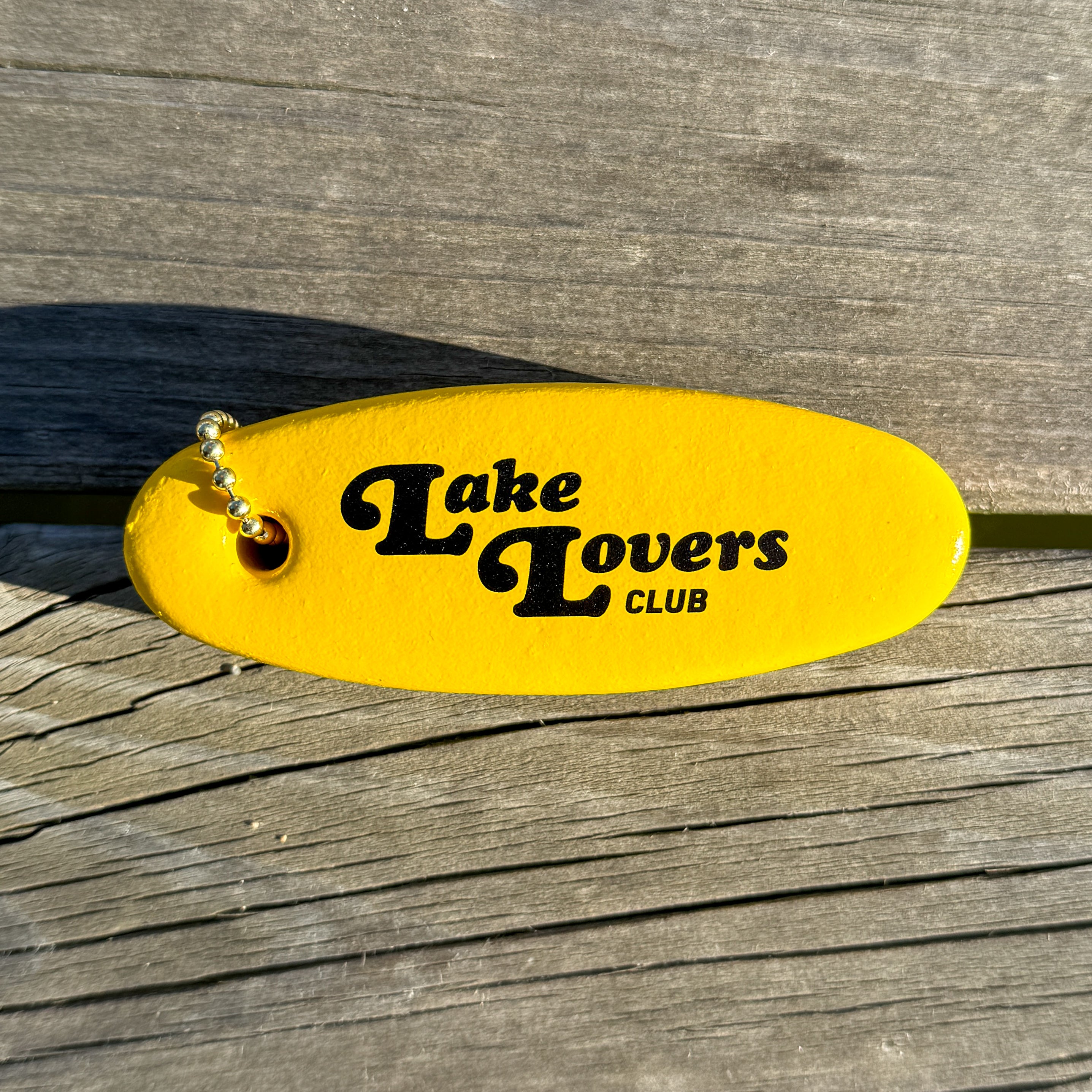 Yellow floater keychain with 'Lake Lovers Club' text on a wooden dock surface.