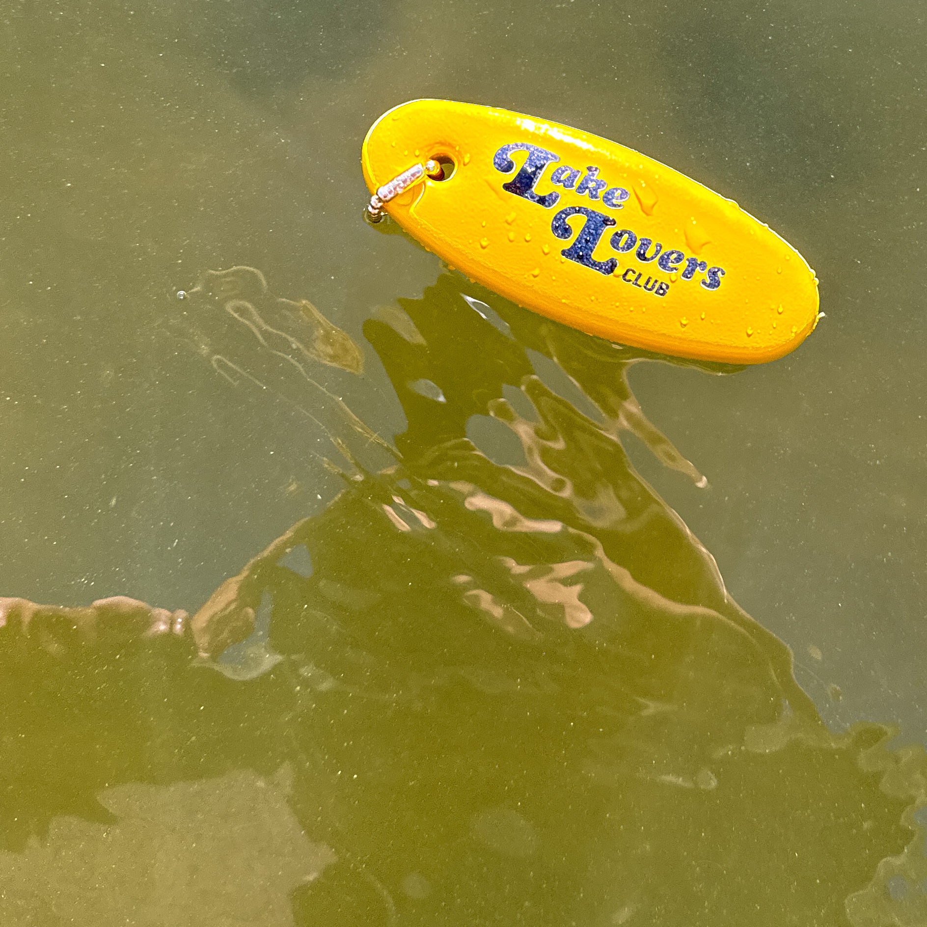 Yellow floaty keychain with 'Lake Lovers Club' text floating on water