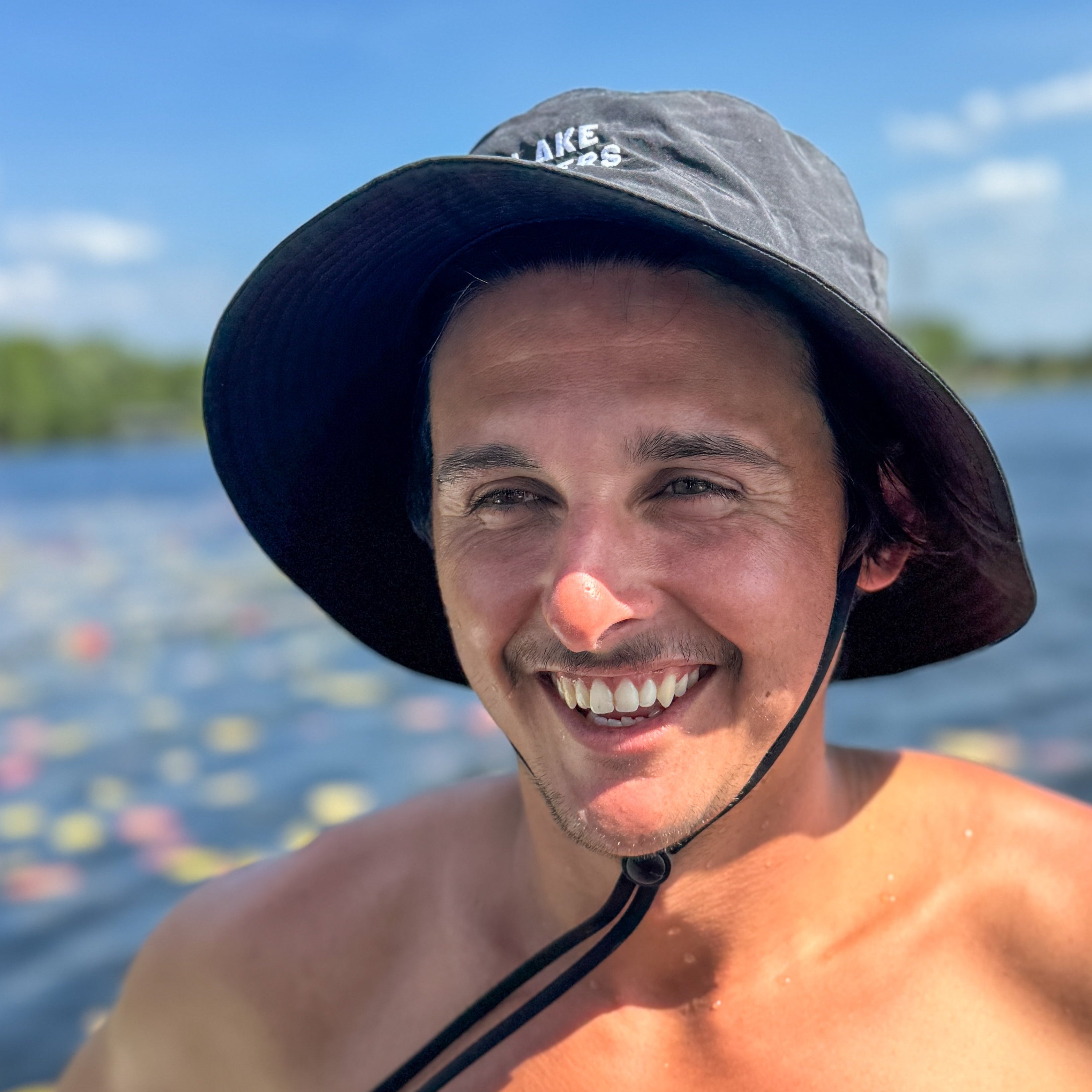 Man wearing a wide-brimmed hat by a lake with colorful buoys.
