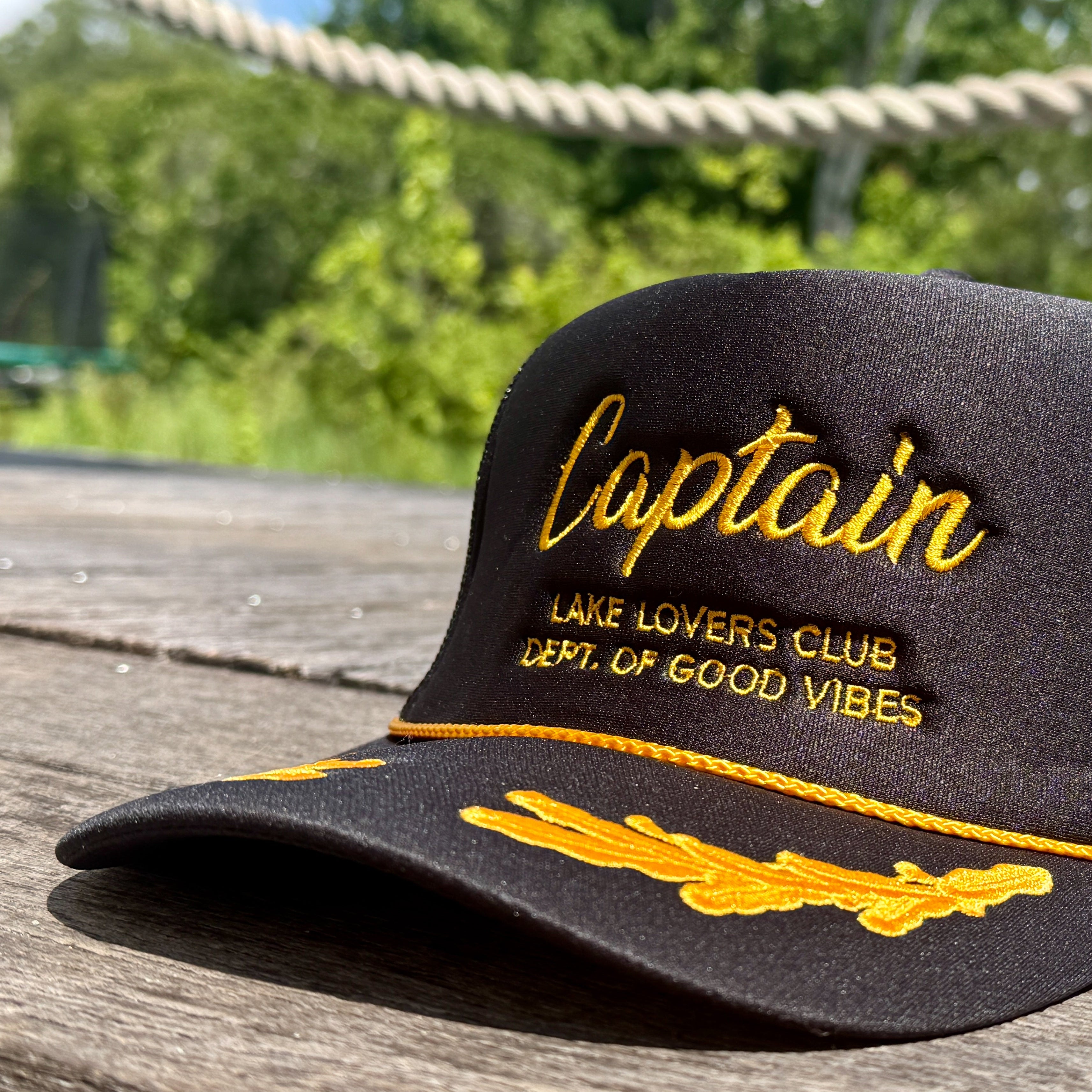 Black cap with yellow text 'Captain' on a wooden surface with greenery in the background