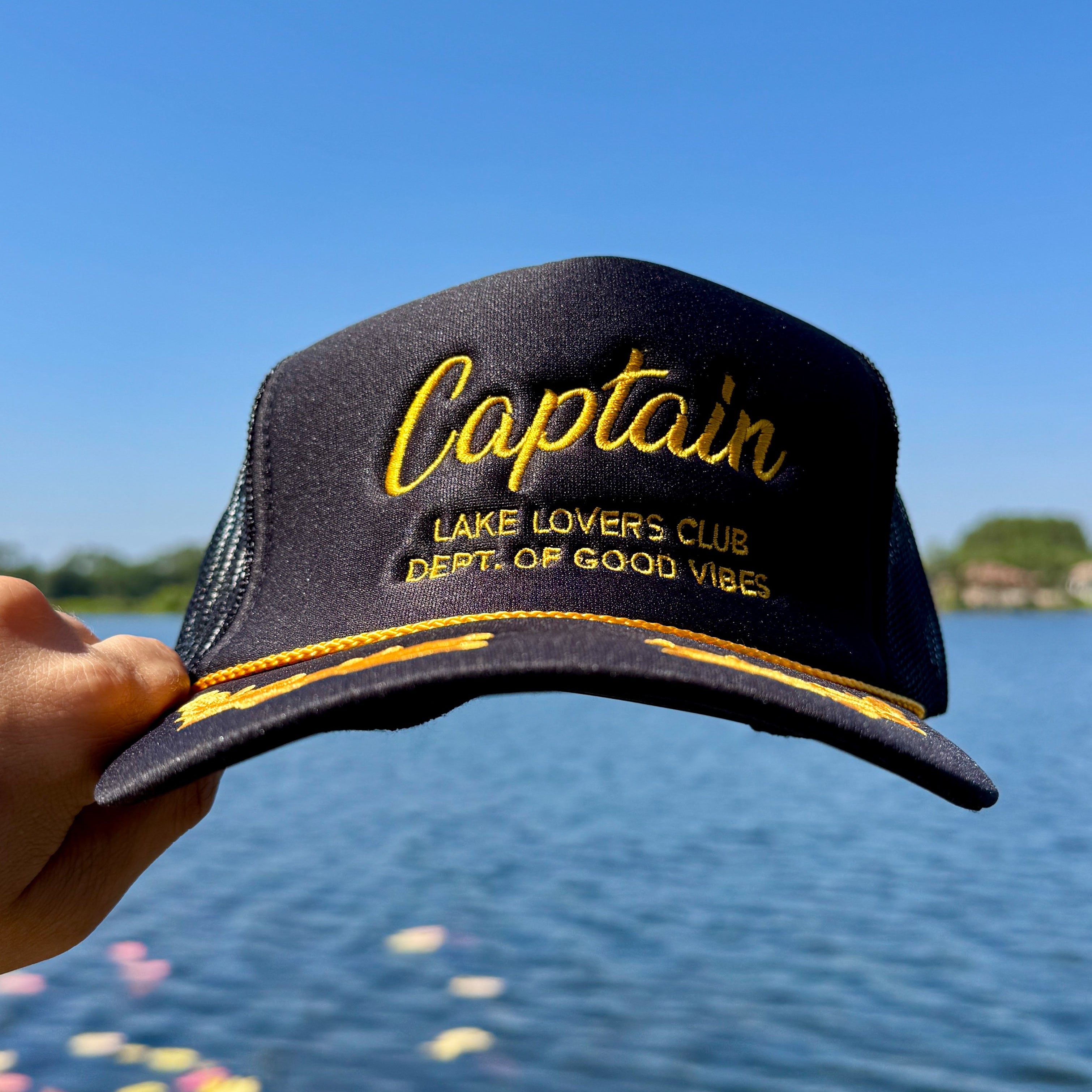 Black cap with yellow text held in front of a lake