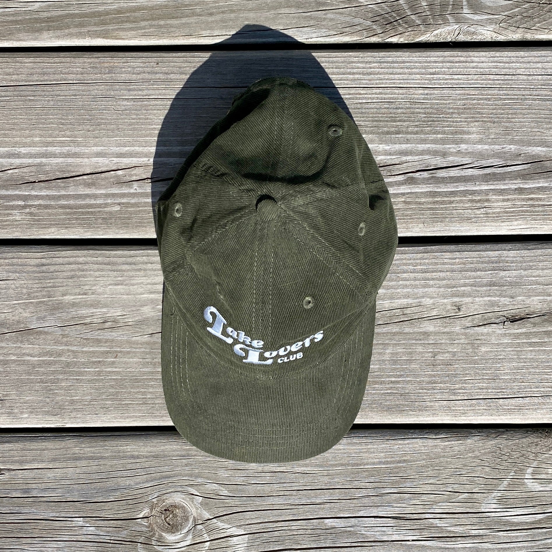 Green cap with 'The Lovers Club' text on a wooden surface