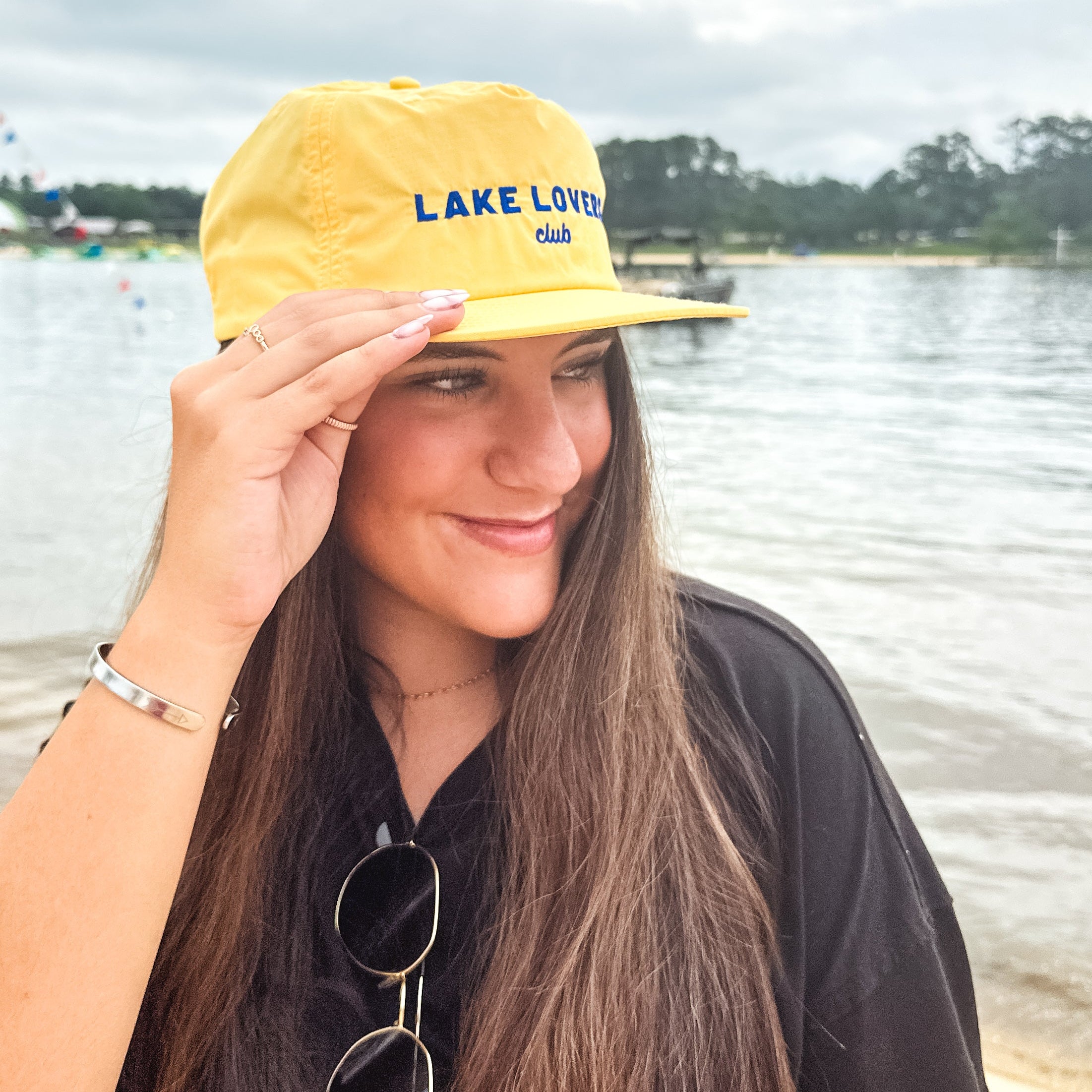 Woman wearing a yellow 'Lake Lover' cap by a body of water