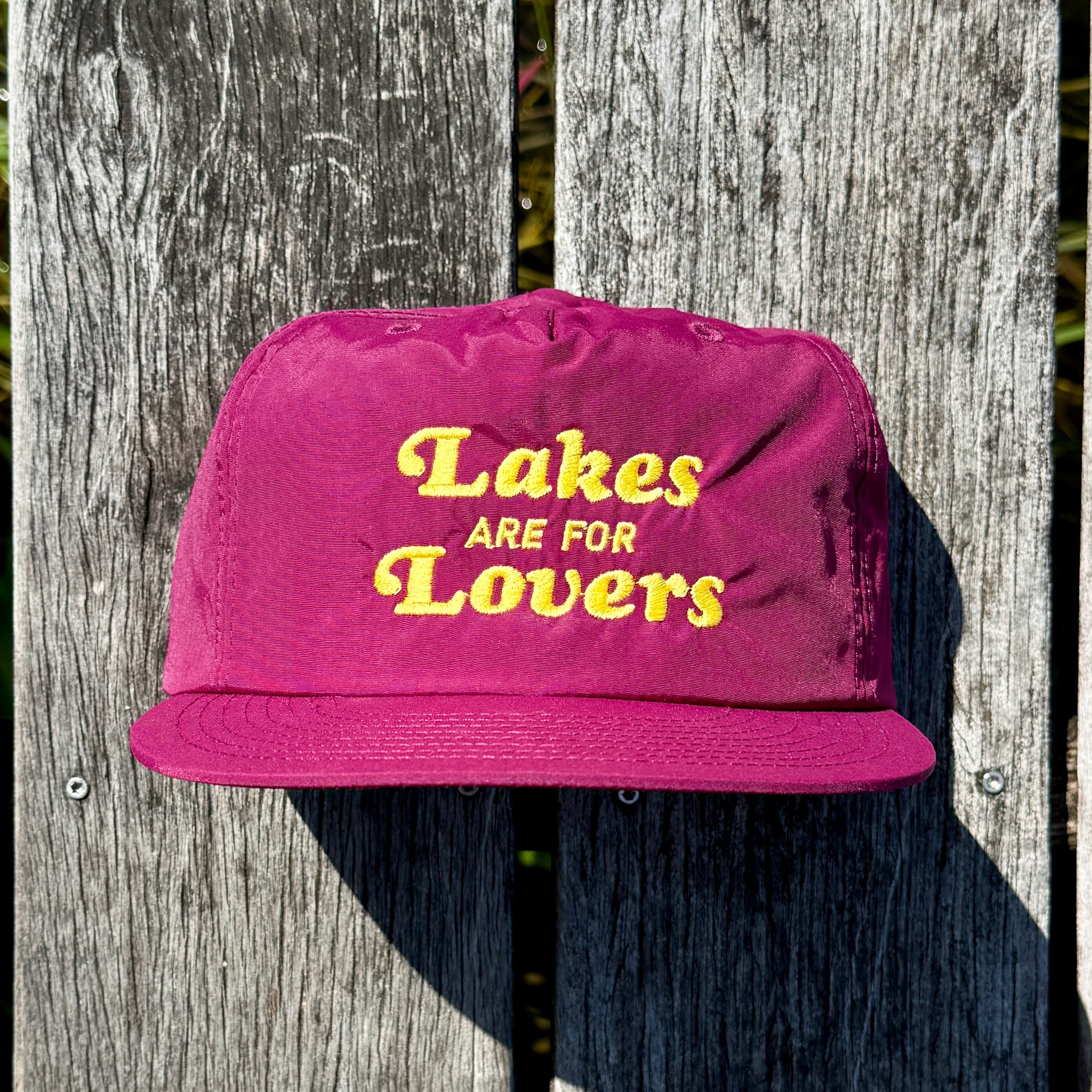 Maroon cap with 'Lakes are for Lovers' text on a wooden surface