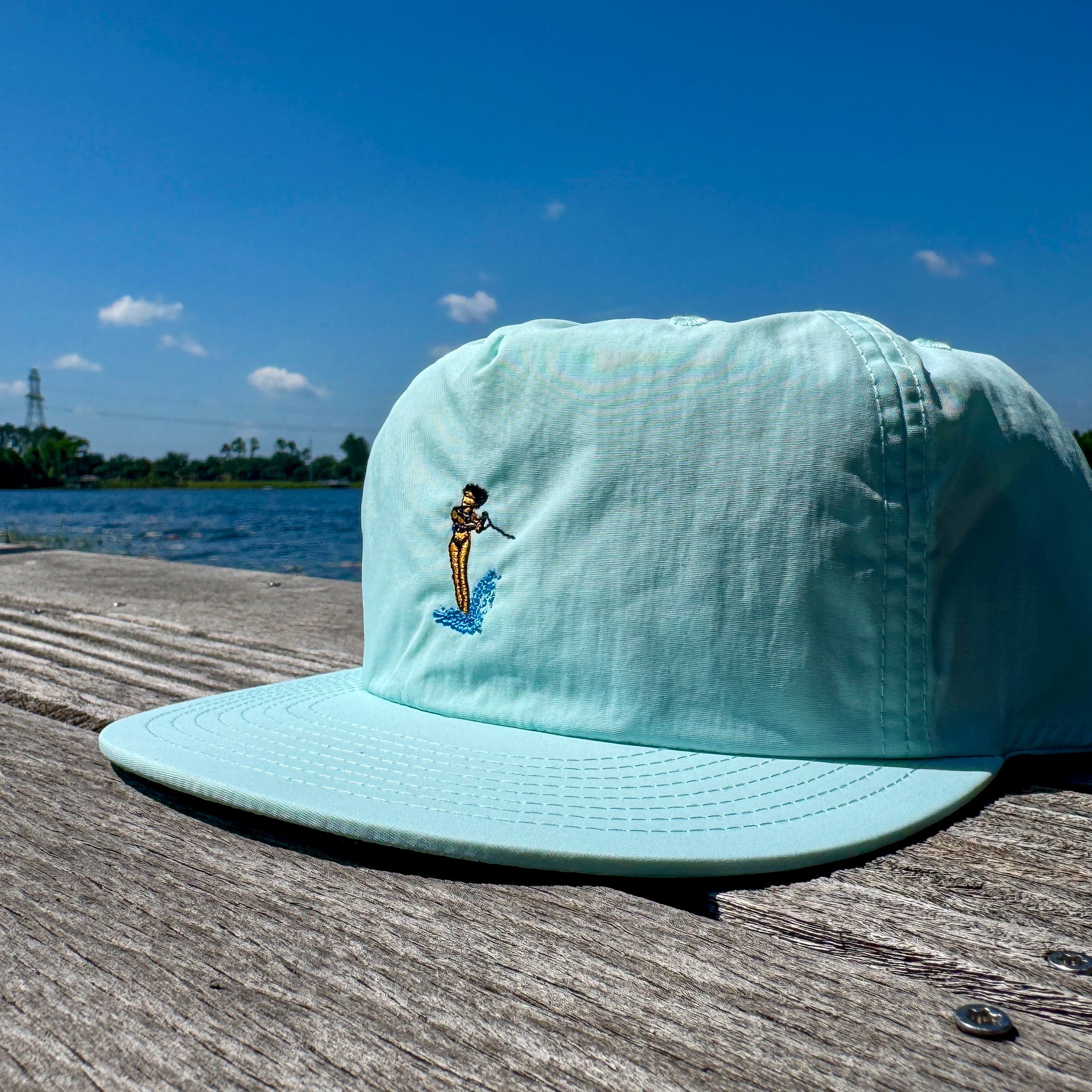 Light blue cap with a small embroidered design on a wooden dock by a lake.