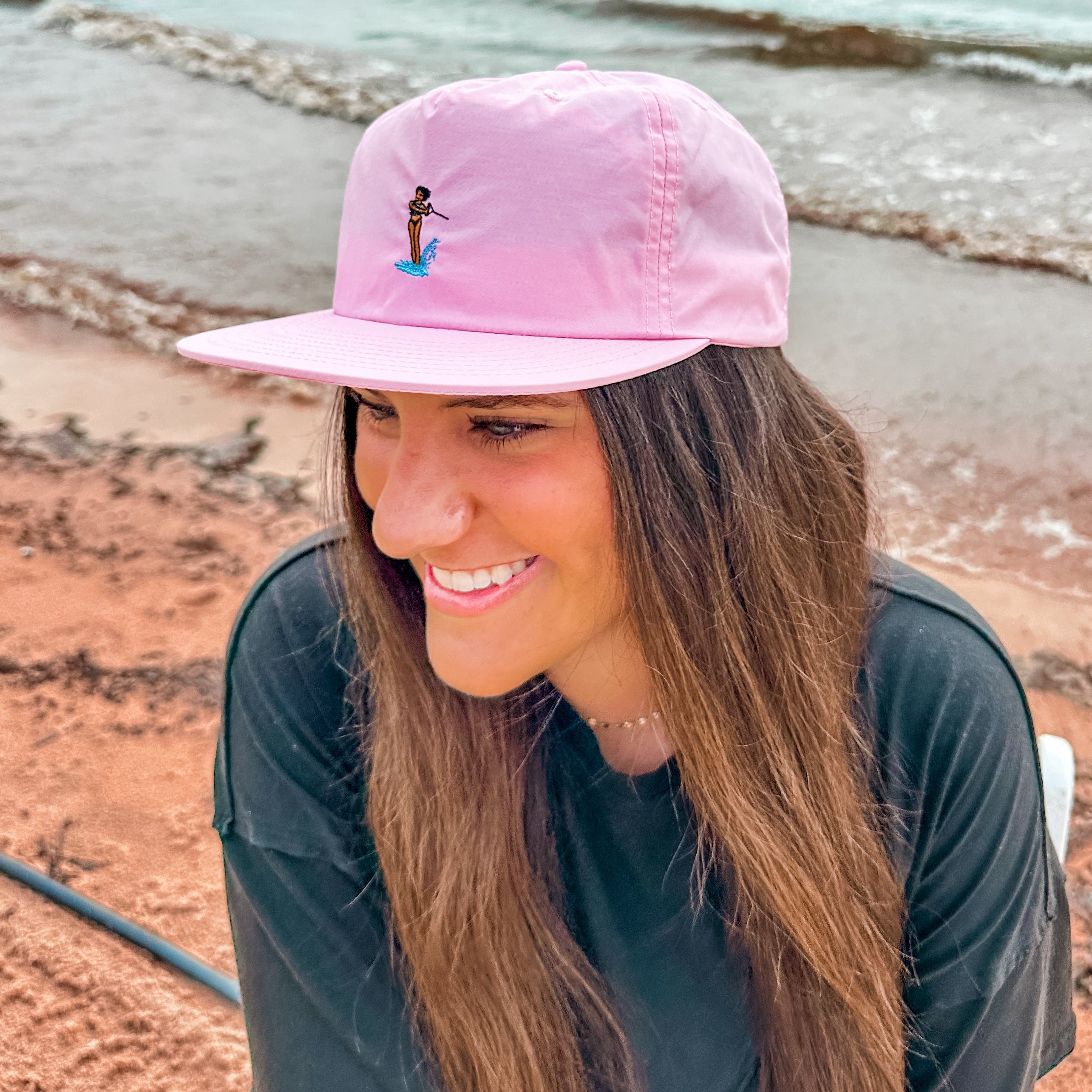 Woman wearing a pink cap with a design by a lake