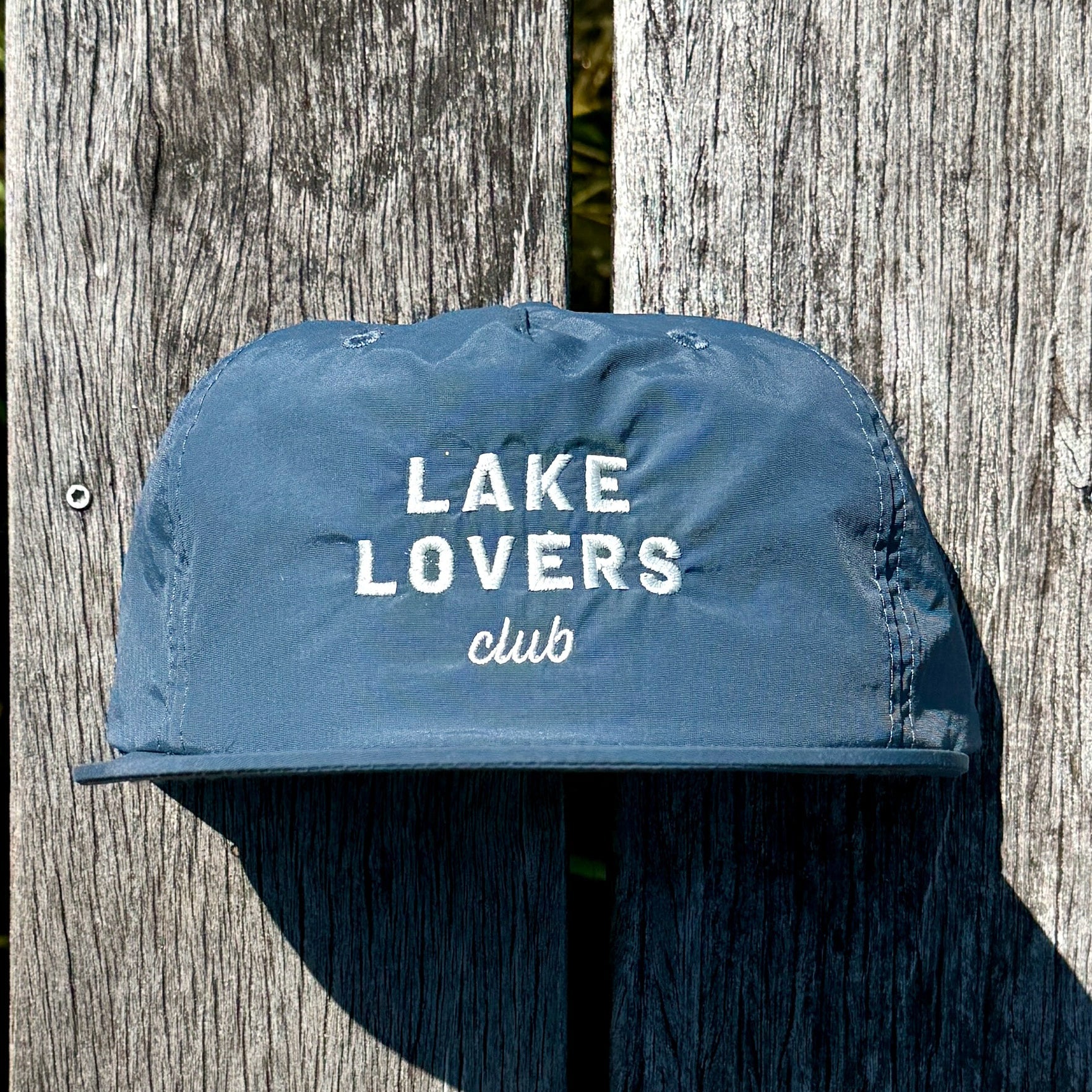 Blue cap with 'Lake Lovers club' text on a wooden surface
