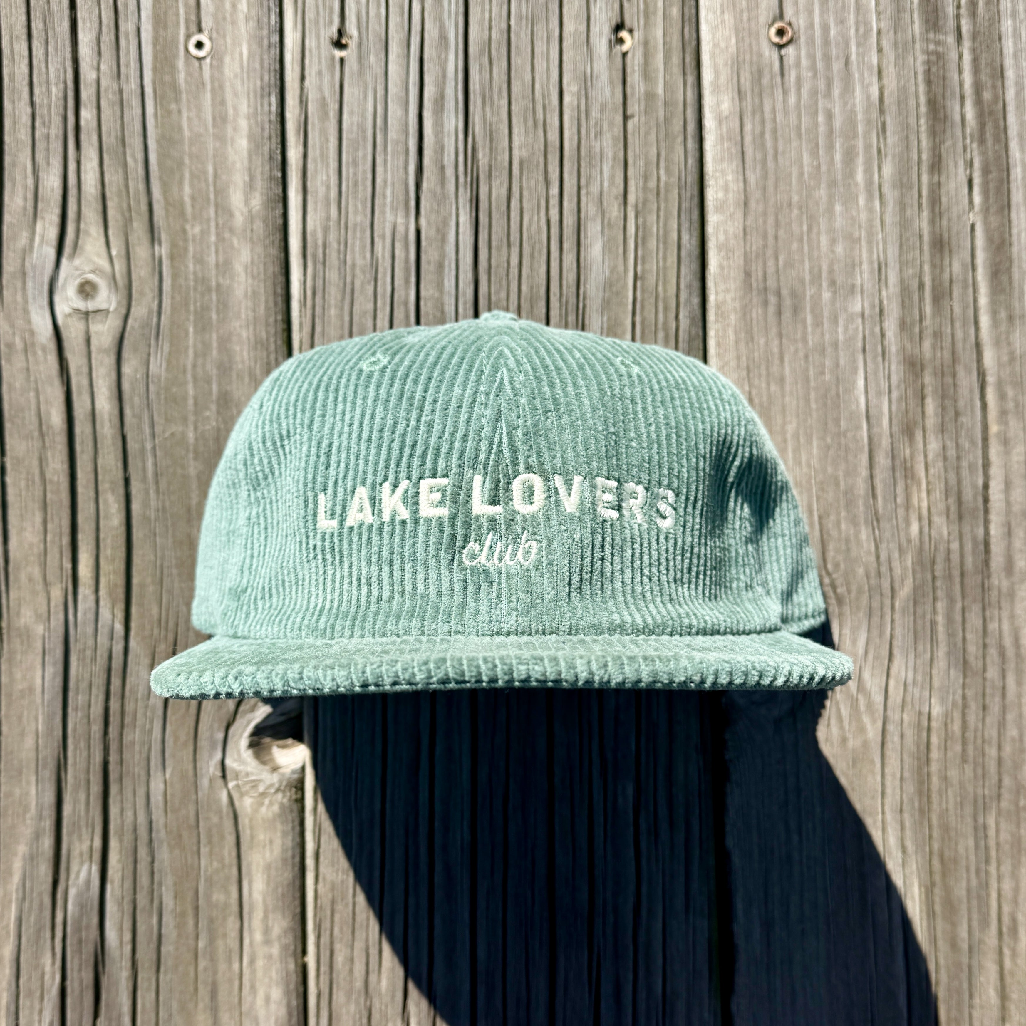 Green cap with 'Lake Lovers Club' text against a wooden background