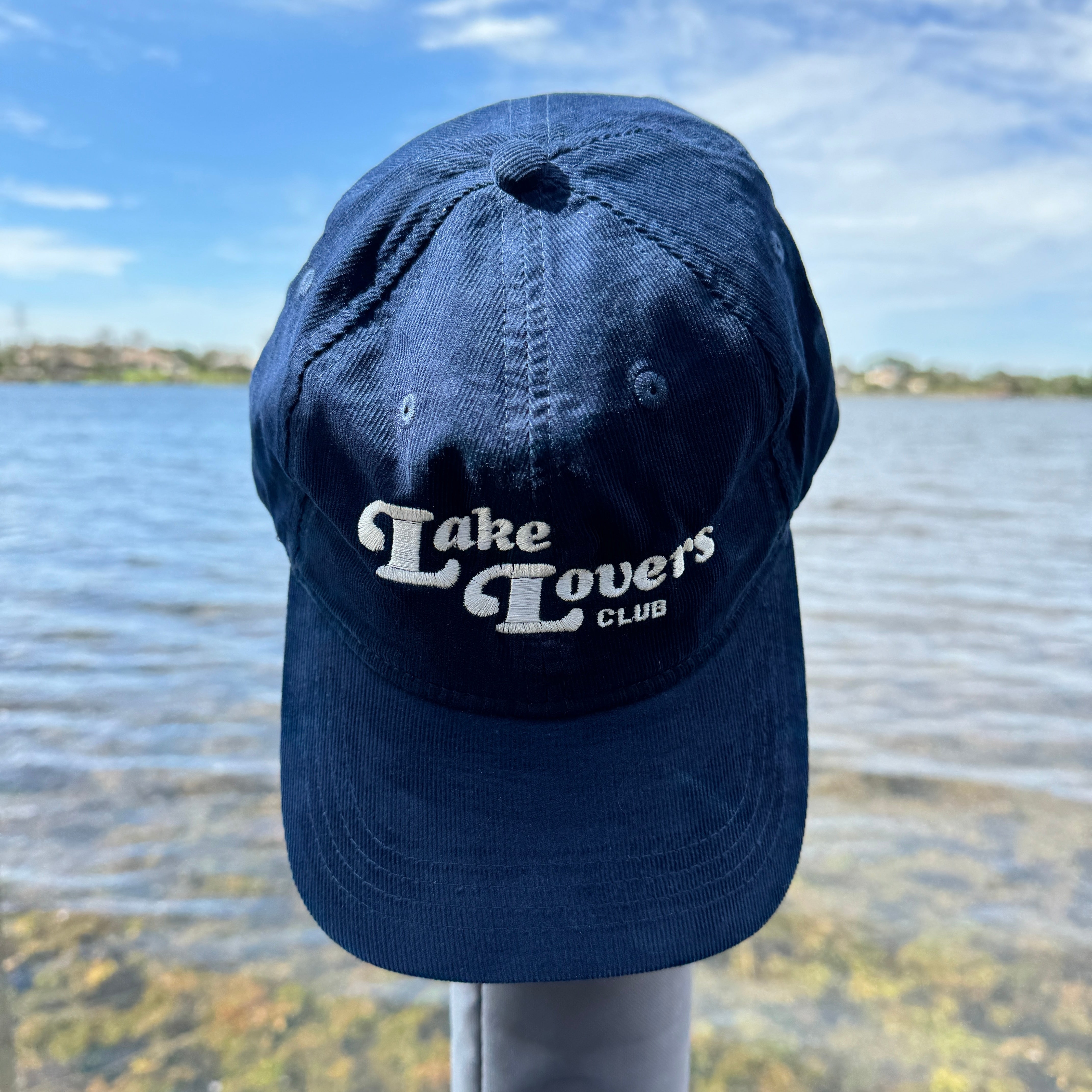 Navy blue cap with 'Lake Lovers Club' text against a lake background