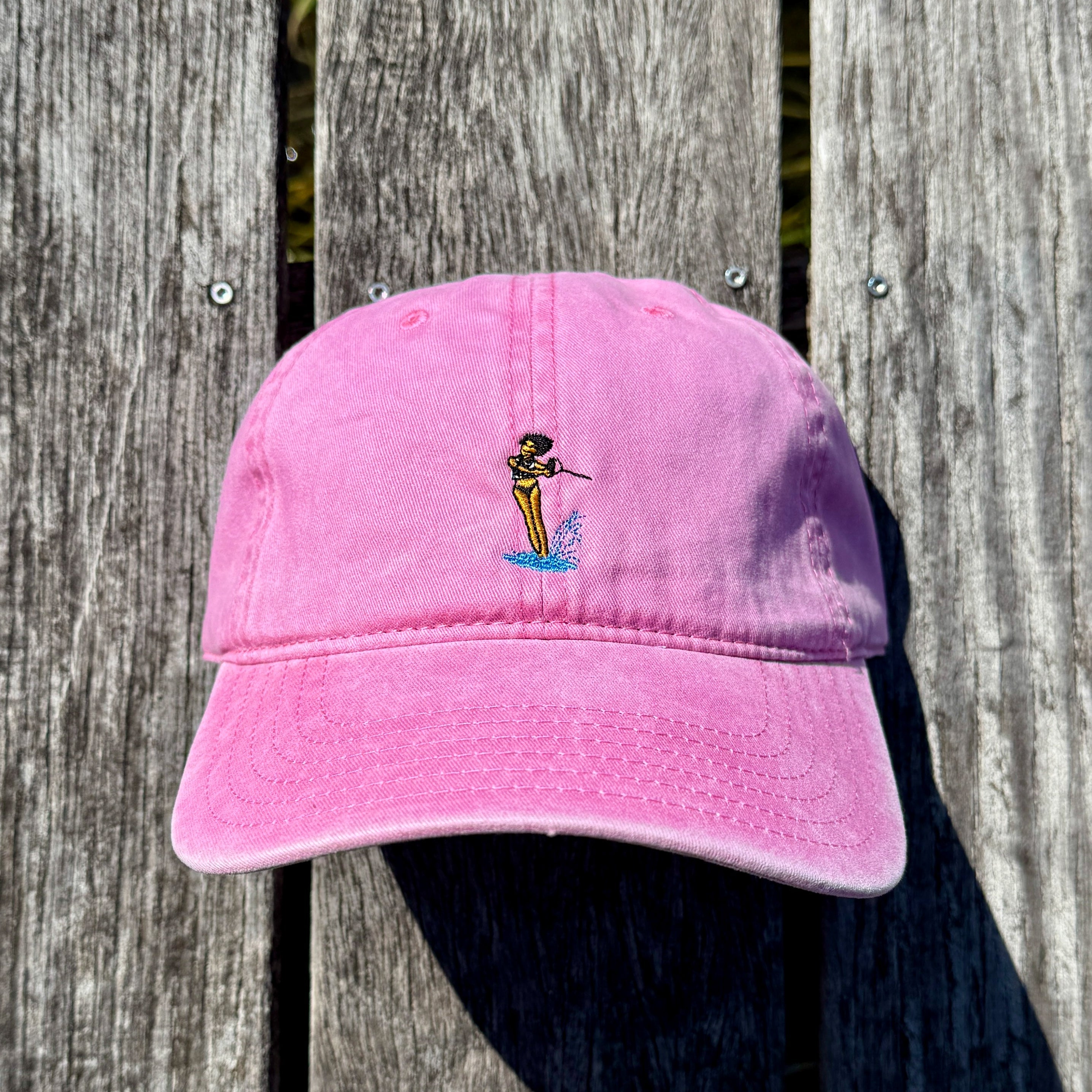 Pink hat on a dock with a waterski girl design embroidered on the front of it.