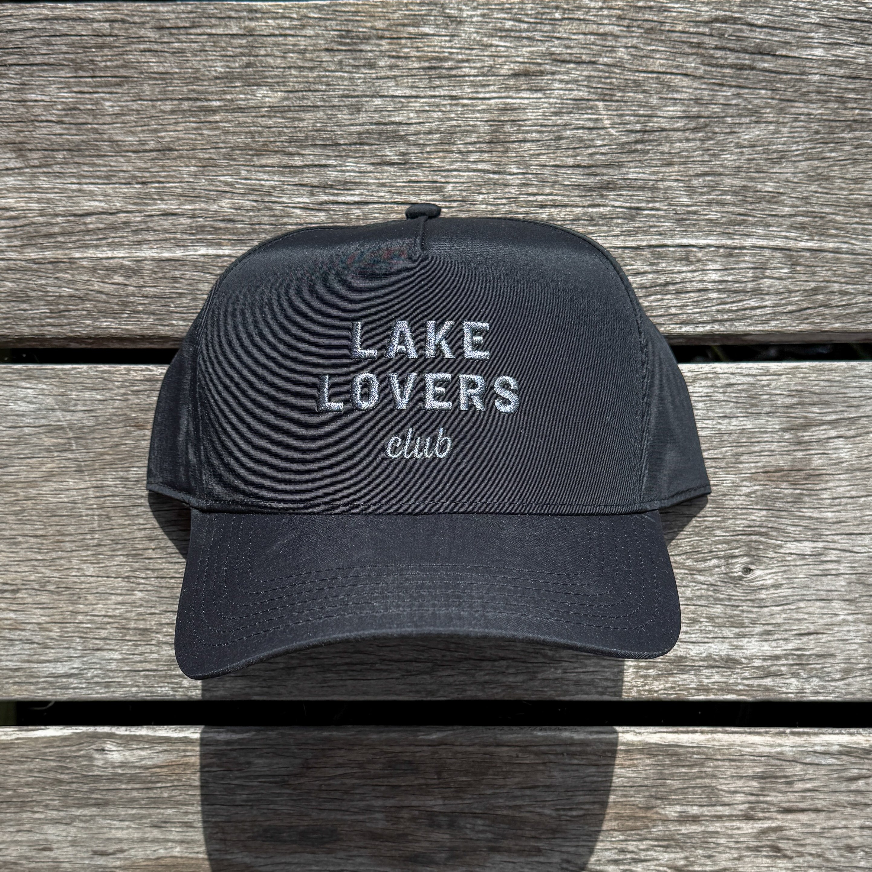 Black cap with 'Lake Lovers Club' text on a wooden surface