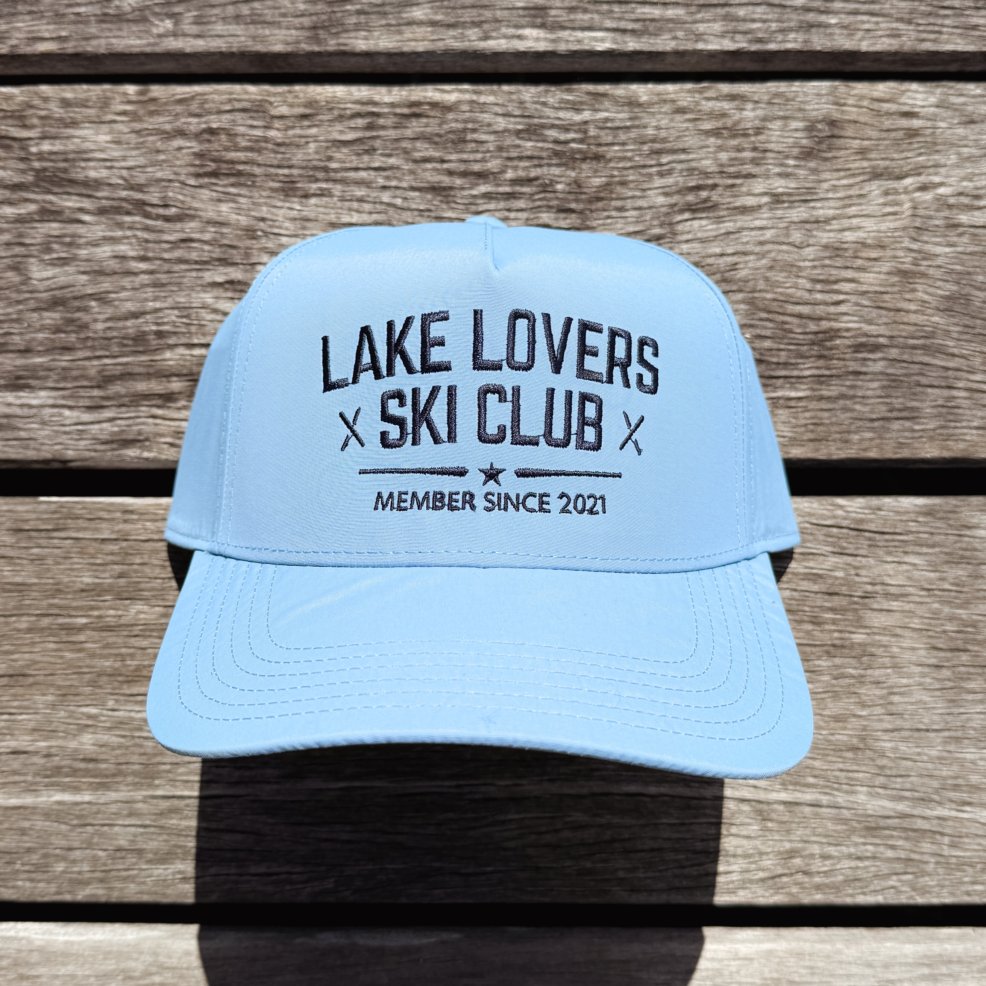 Light blue cap with 'Lake Lovers Ski Club' text on a wooden surface