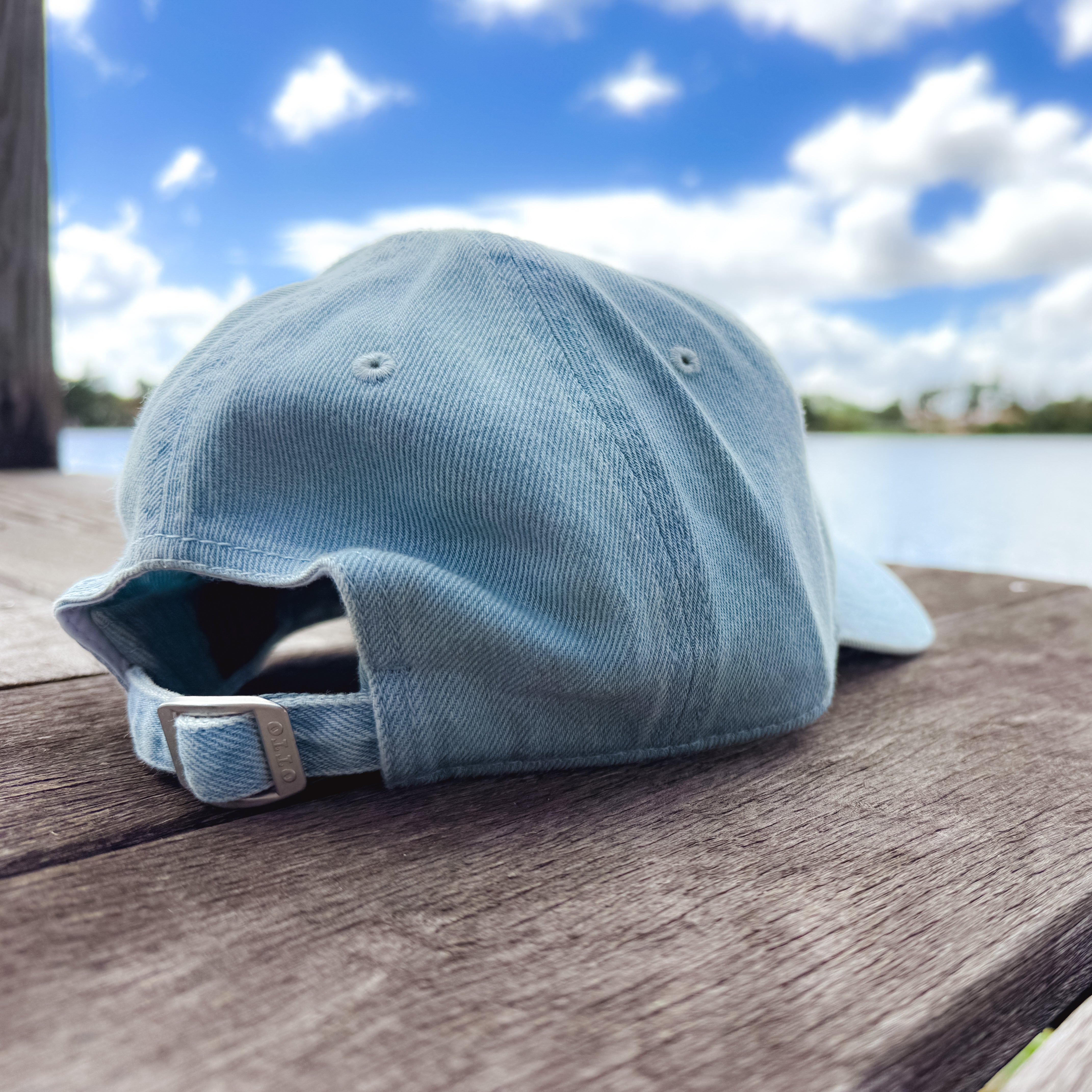 The back of a denim hat lying on a dock with a lake and trees in the background.