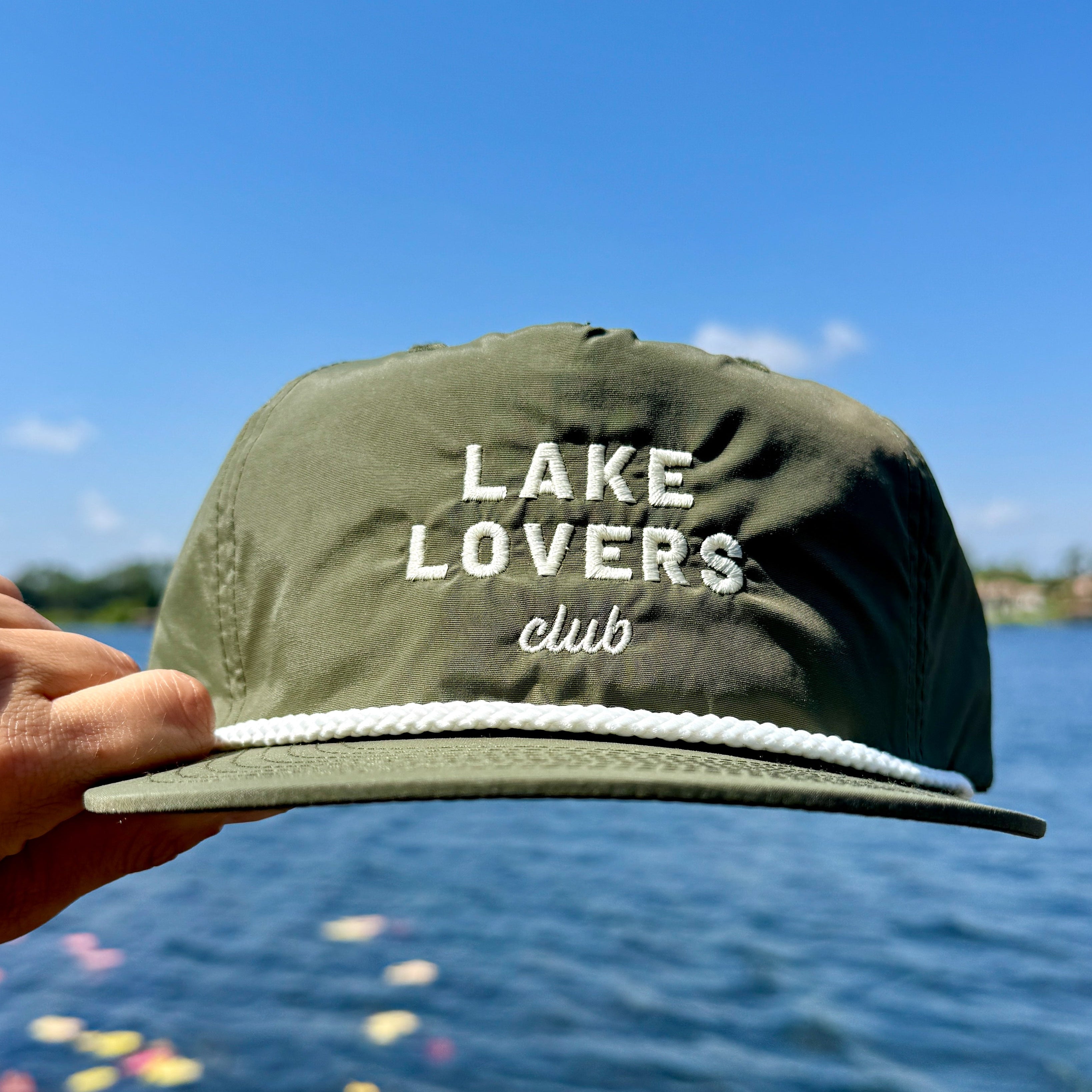 Green cap with 'Lake Lovers Club' text held by a hand against a lake background