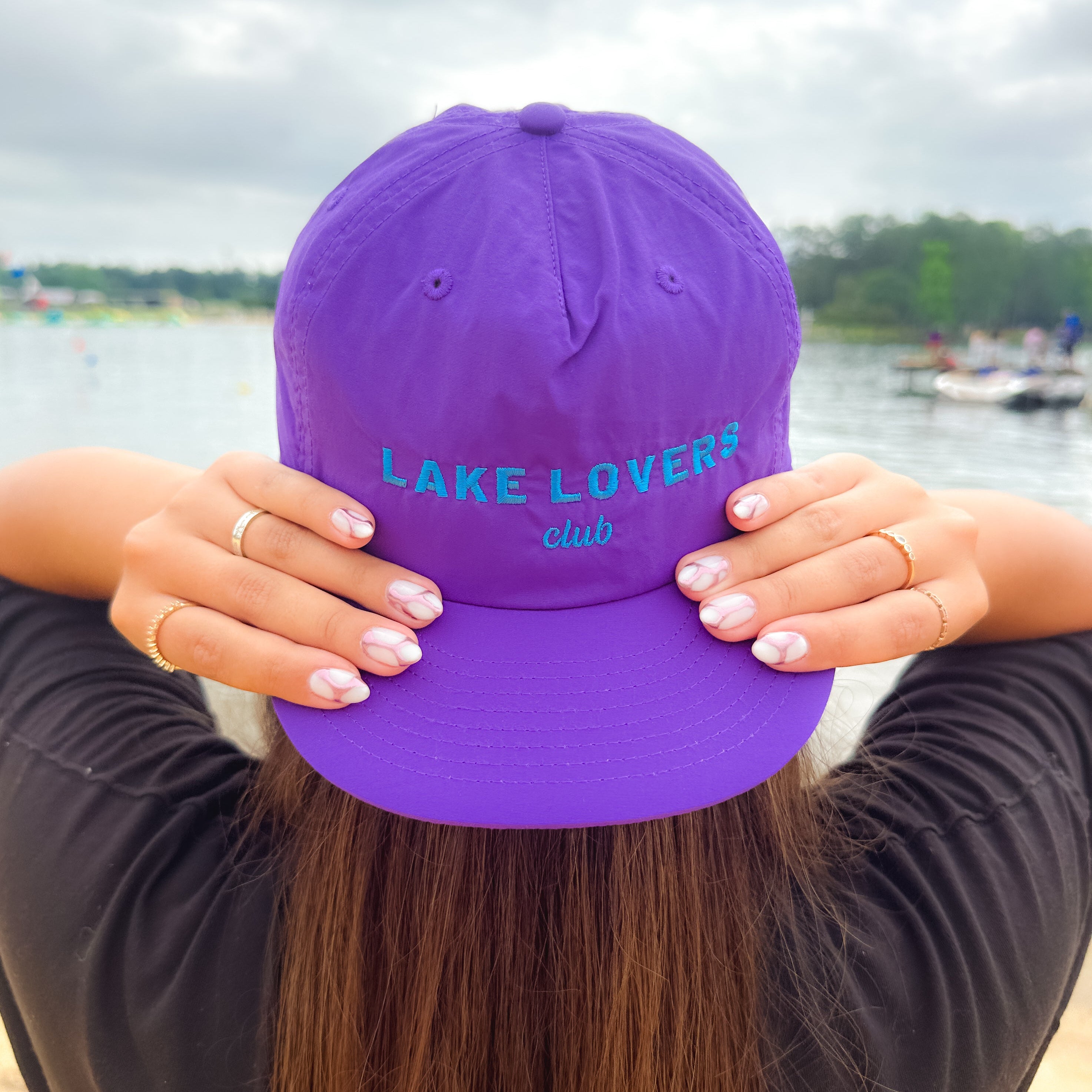 Purple cap with 'Lake Lovers Club' text held by a person at a lakeside.