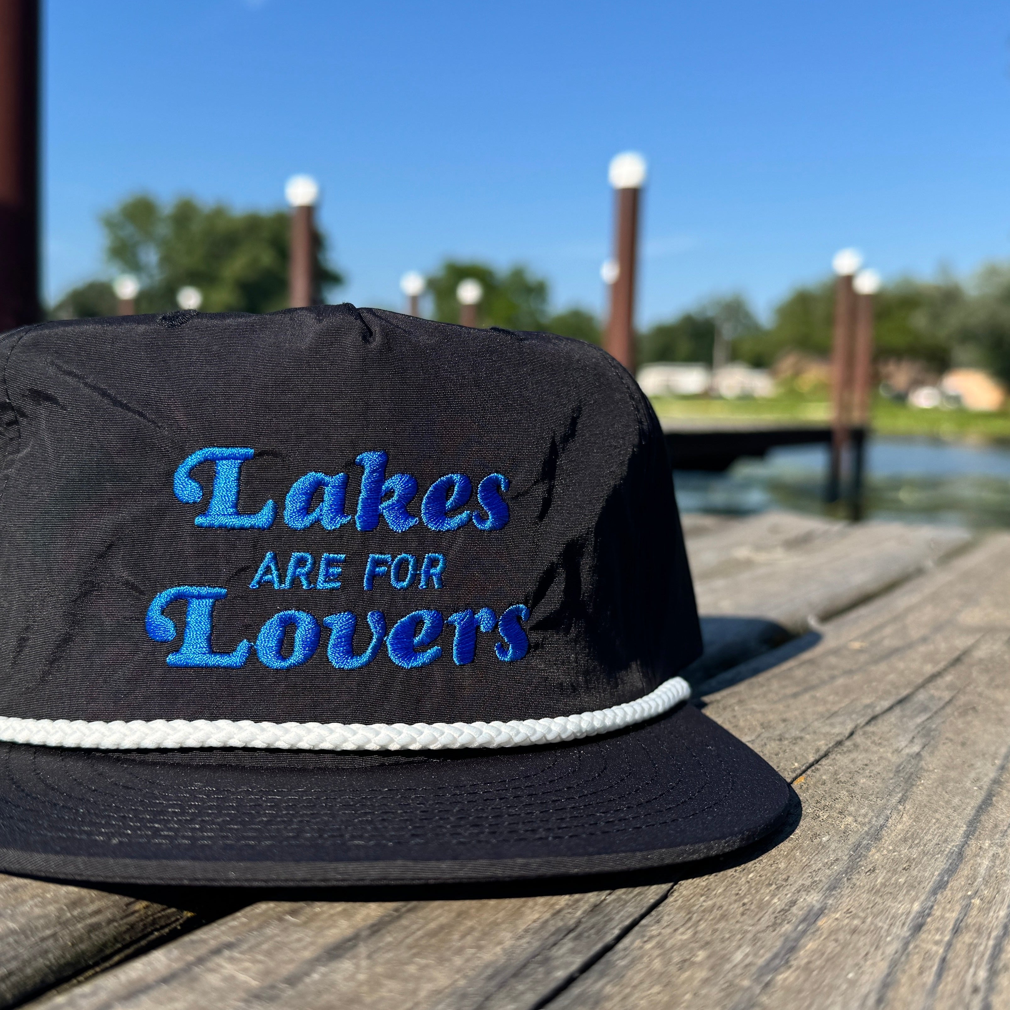 Black rope hat on a dock that says Lakes are for Lovers in blue thread.