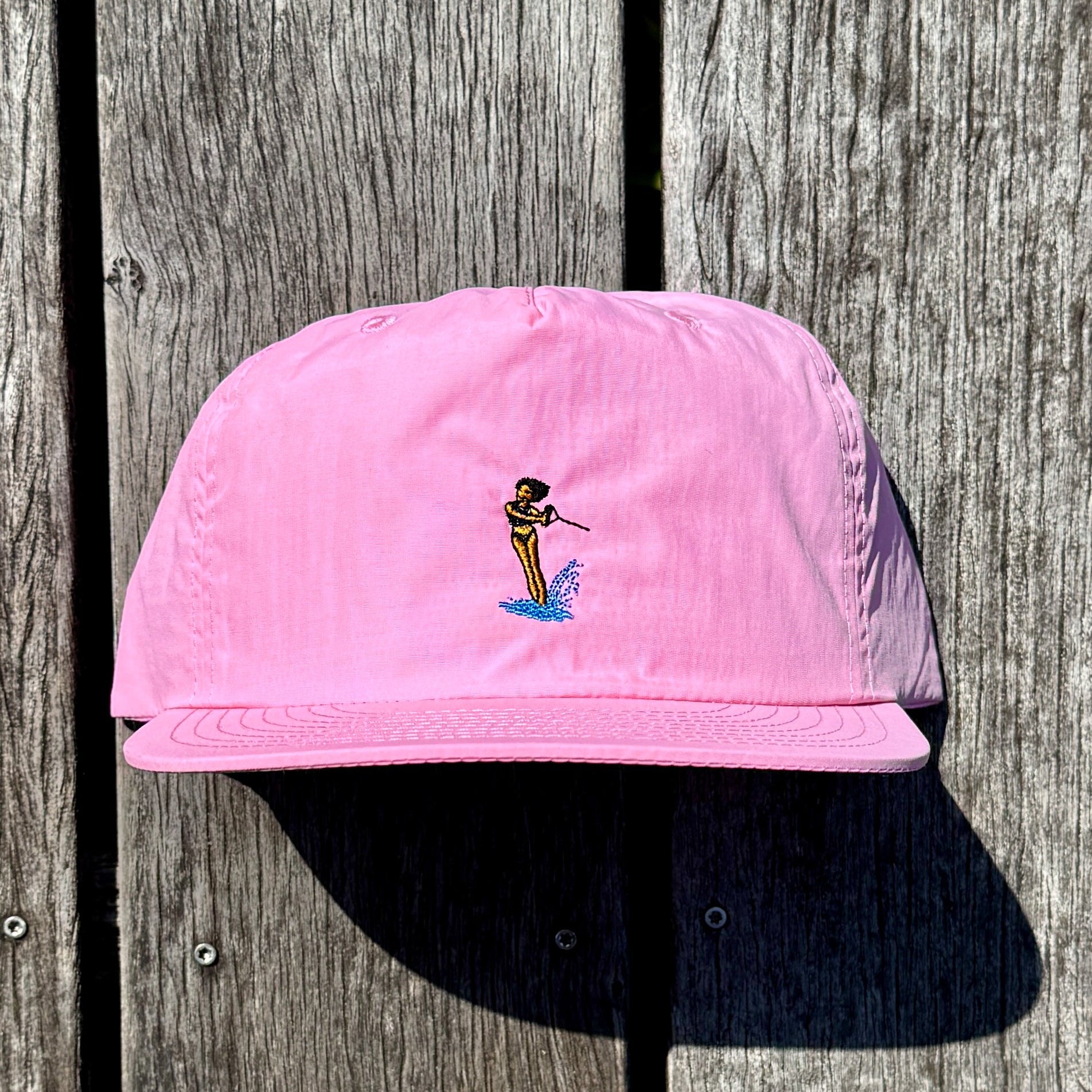 Pink cap with a small embroidered waterski design on a wooden background