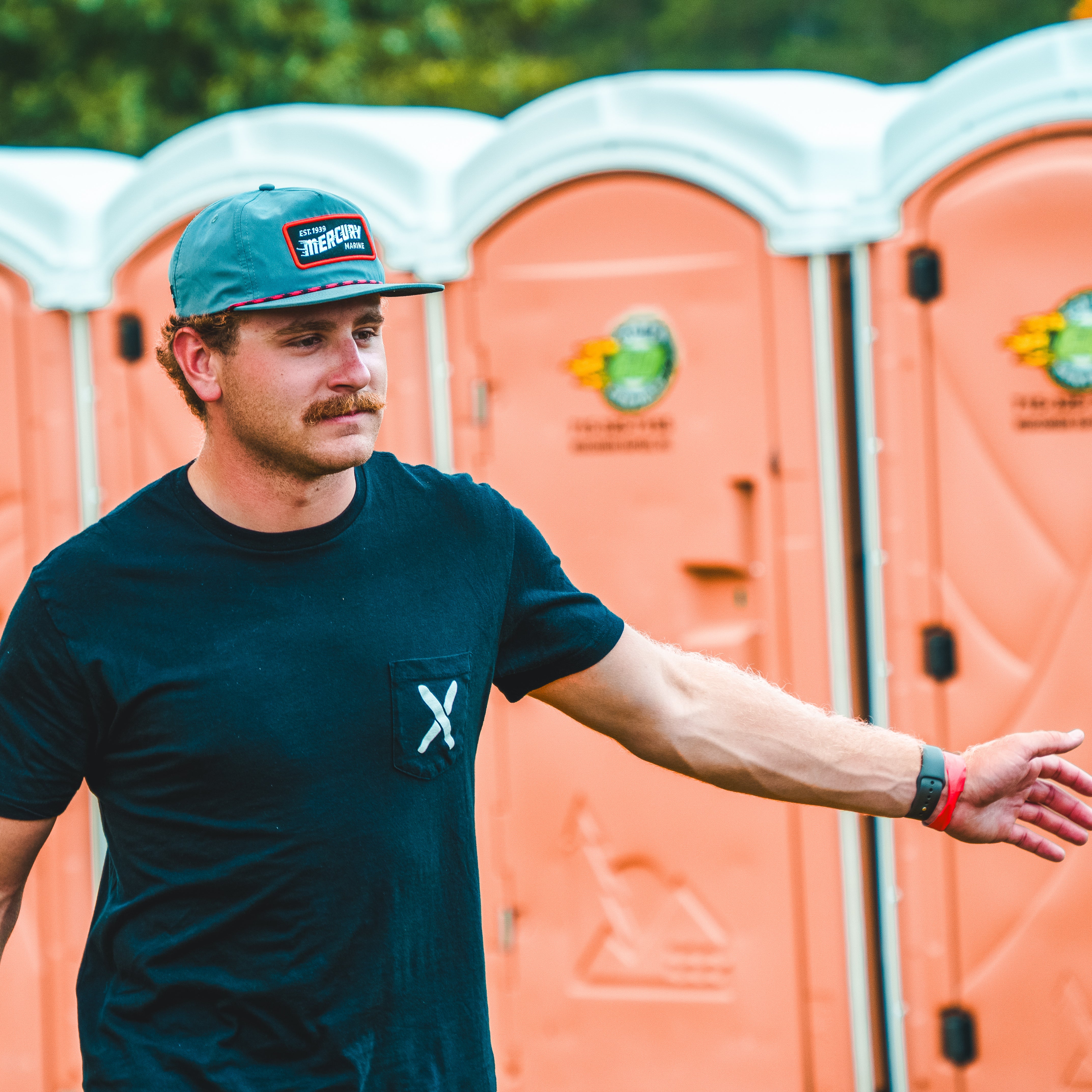 Man wearing a cap and t-shirt standing in front of portable toilets
