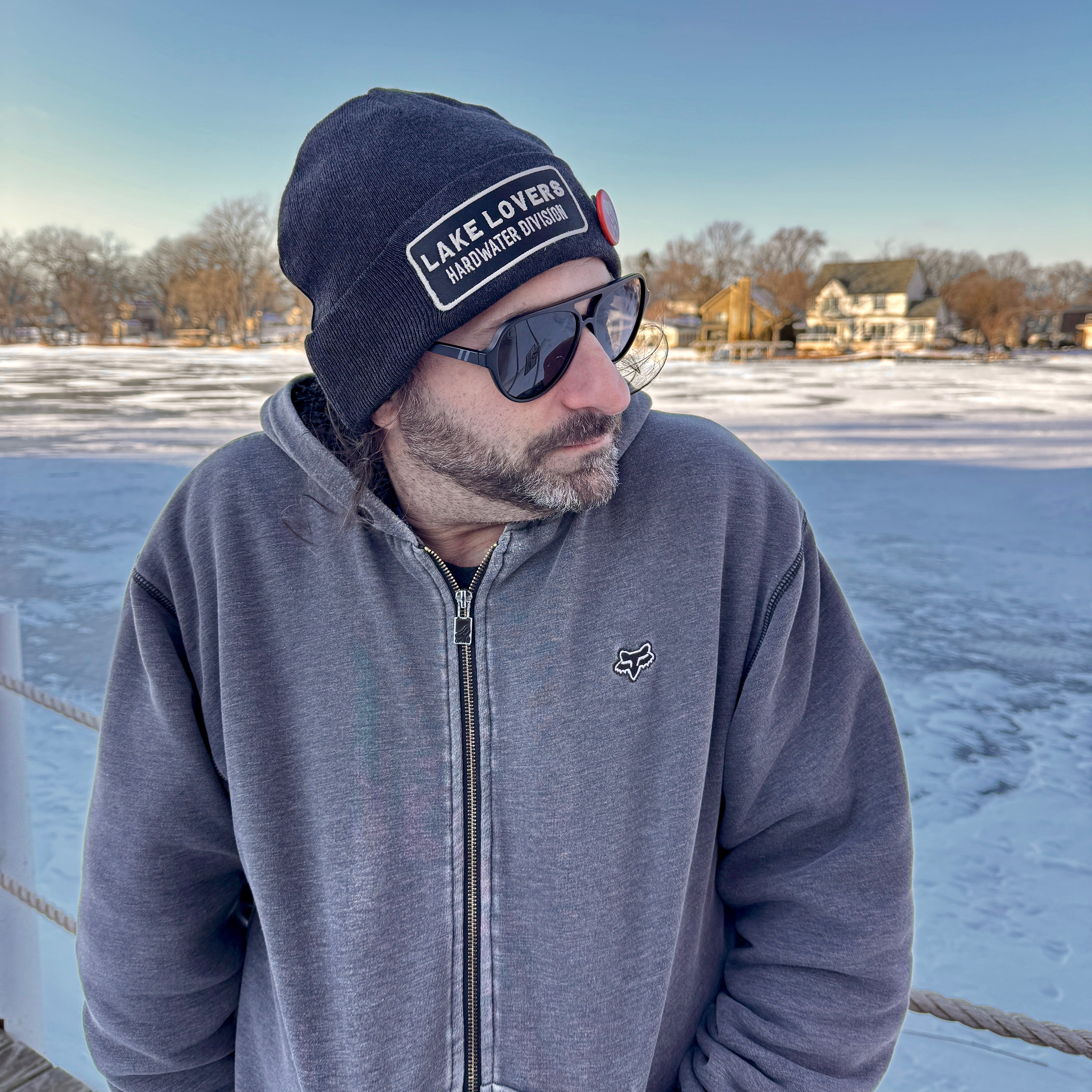 Man wearing a beanie and sunglasses standing on a frozen lake.