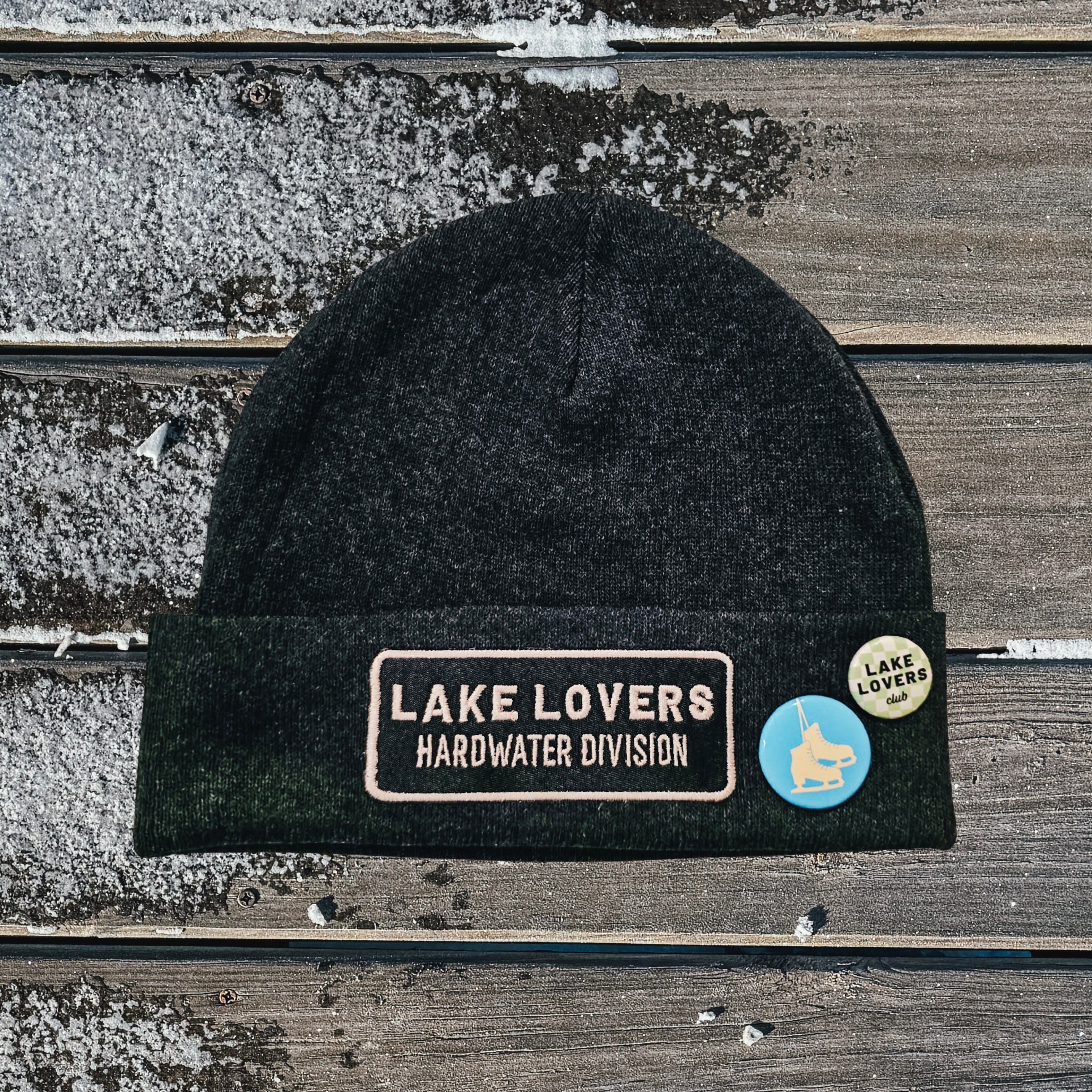 Black beanie with 'Lake Lovers Hardwater Division' patch on a wooden surface
