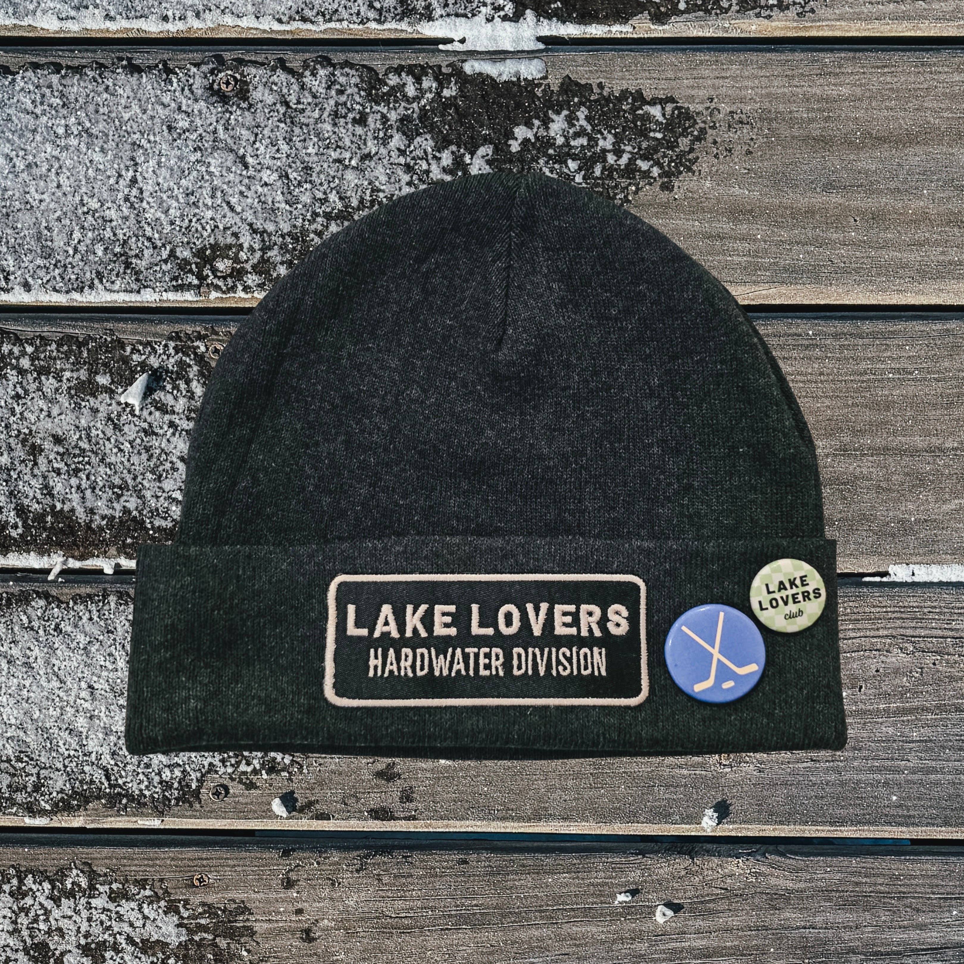 Black beanie with 'Lake Lovers Hardwater Division' patch on a wooden surface