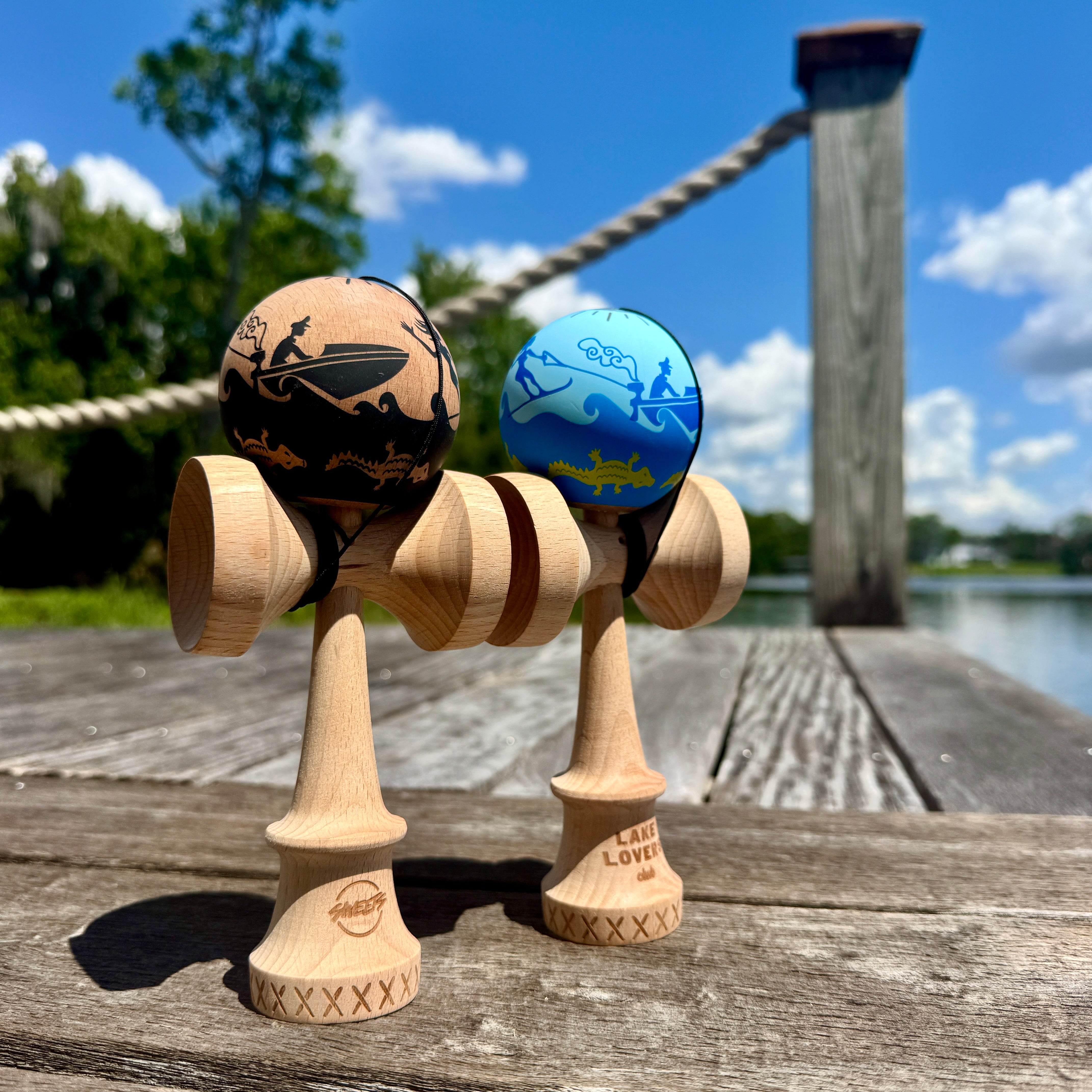Two wooden kendama toys on a wooden surface with a scenic background