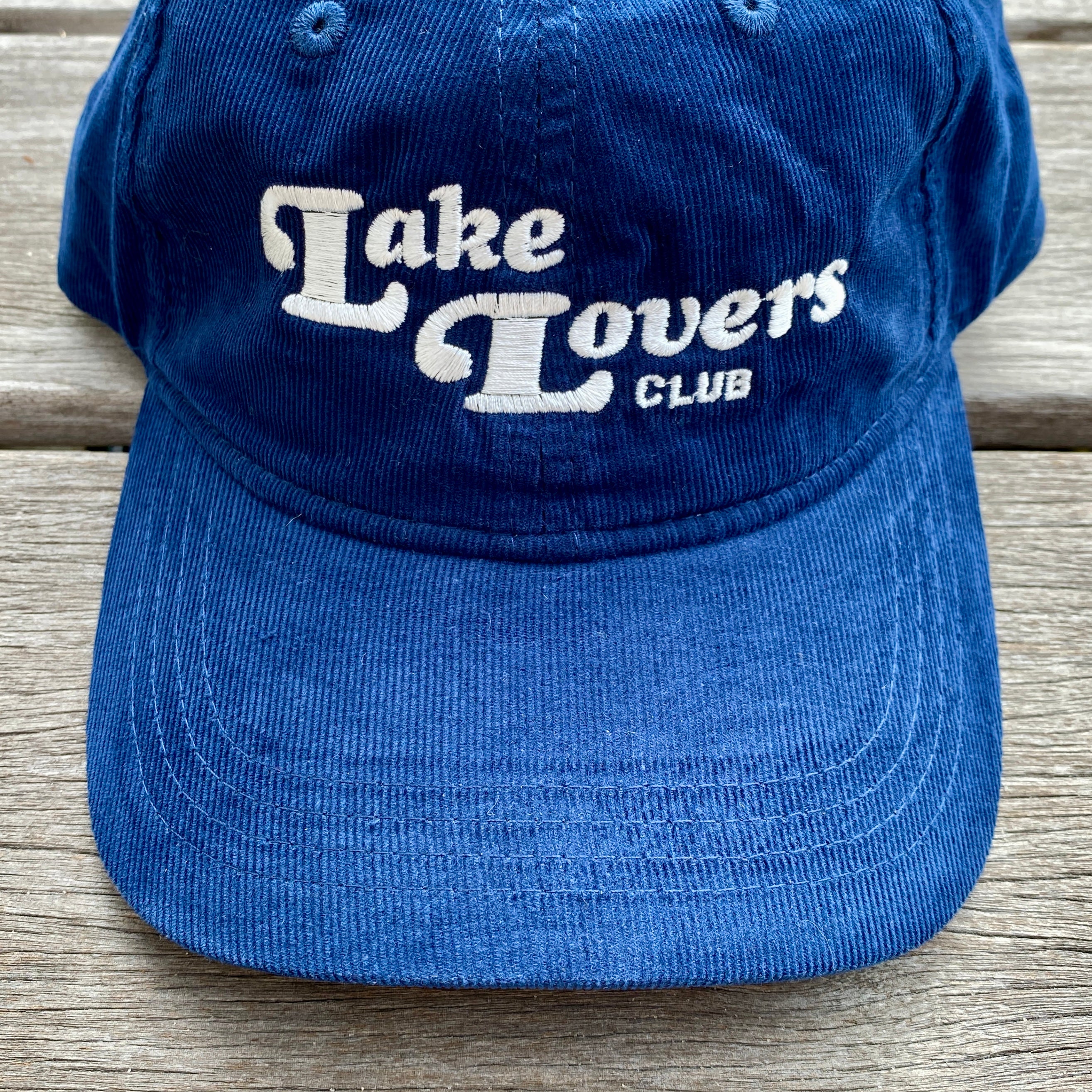 Blue cap with 'Lake Lovers Club' text on a wooden surface