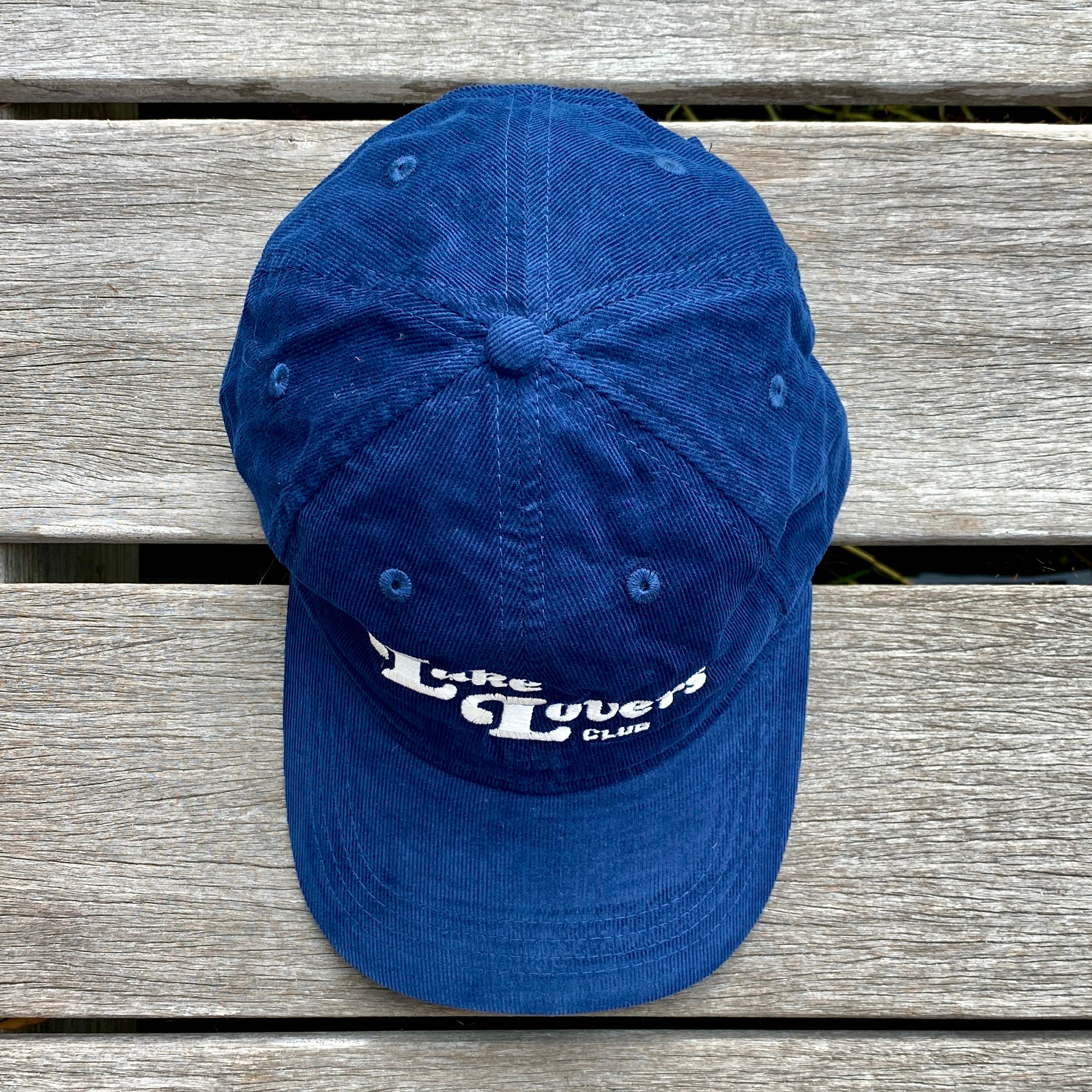 Blue cap with 'Lake Lovers Club' text on a wooden surface