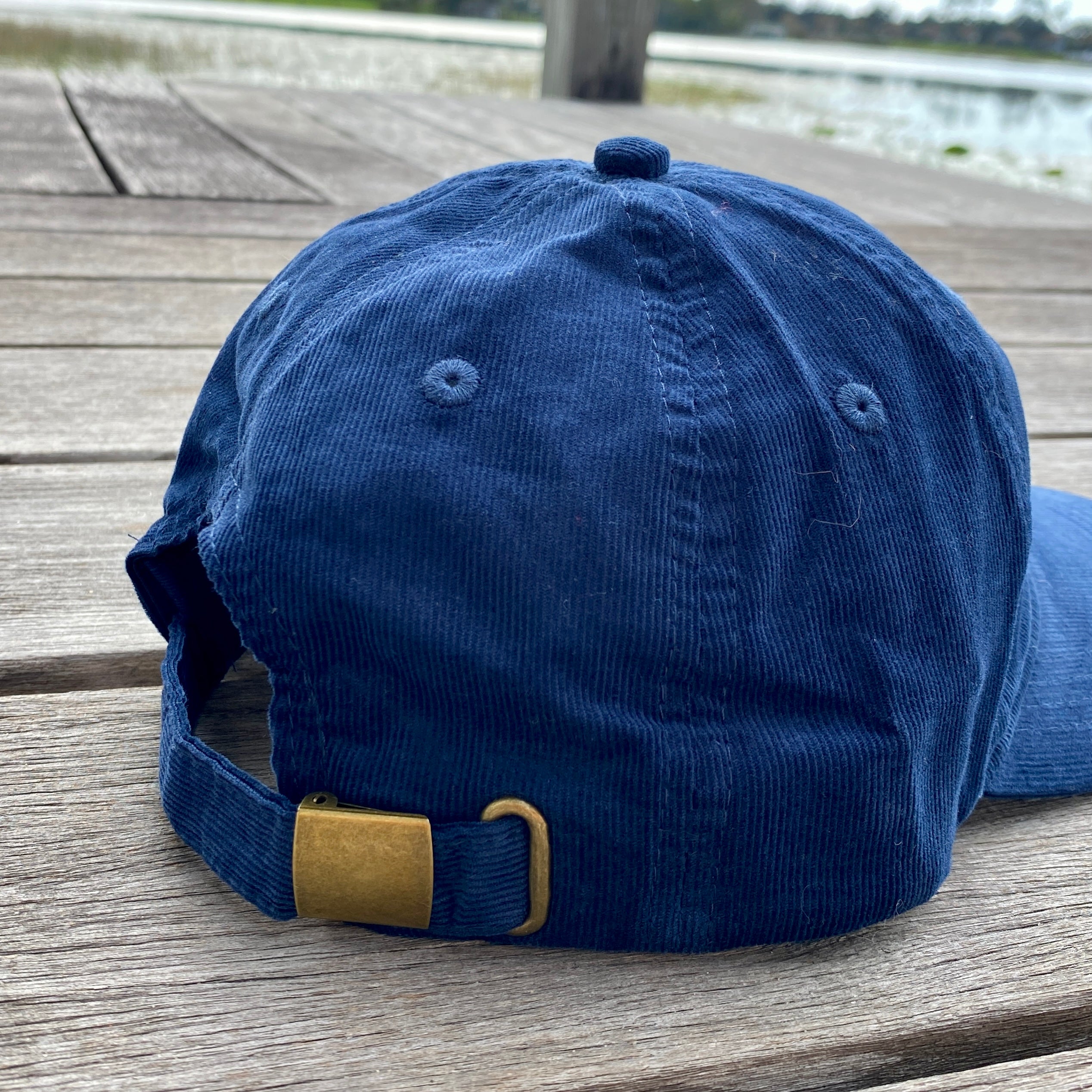 Blue cap with a gold buckle on a wooden surface near a body of water.