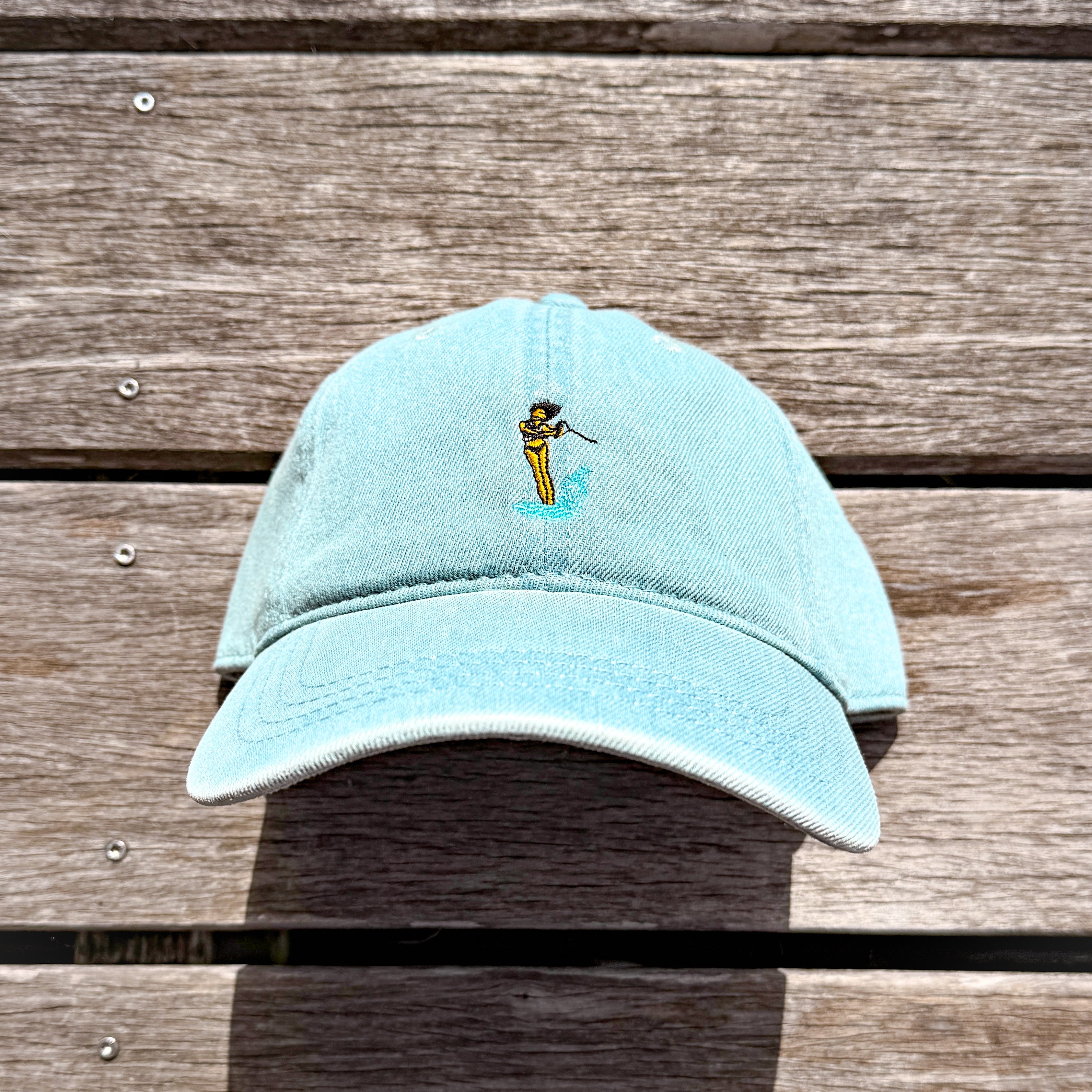 Denim hat on a dock with a waterski girl design embroidered on the front of it.