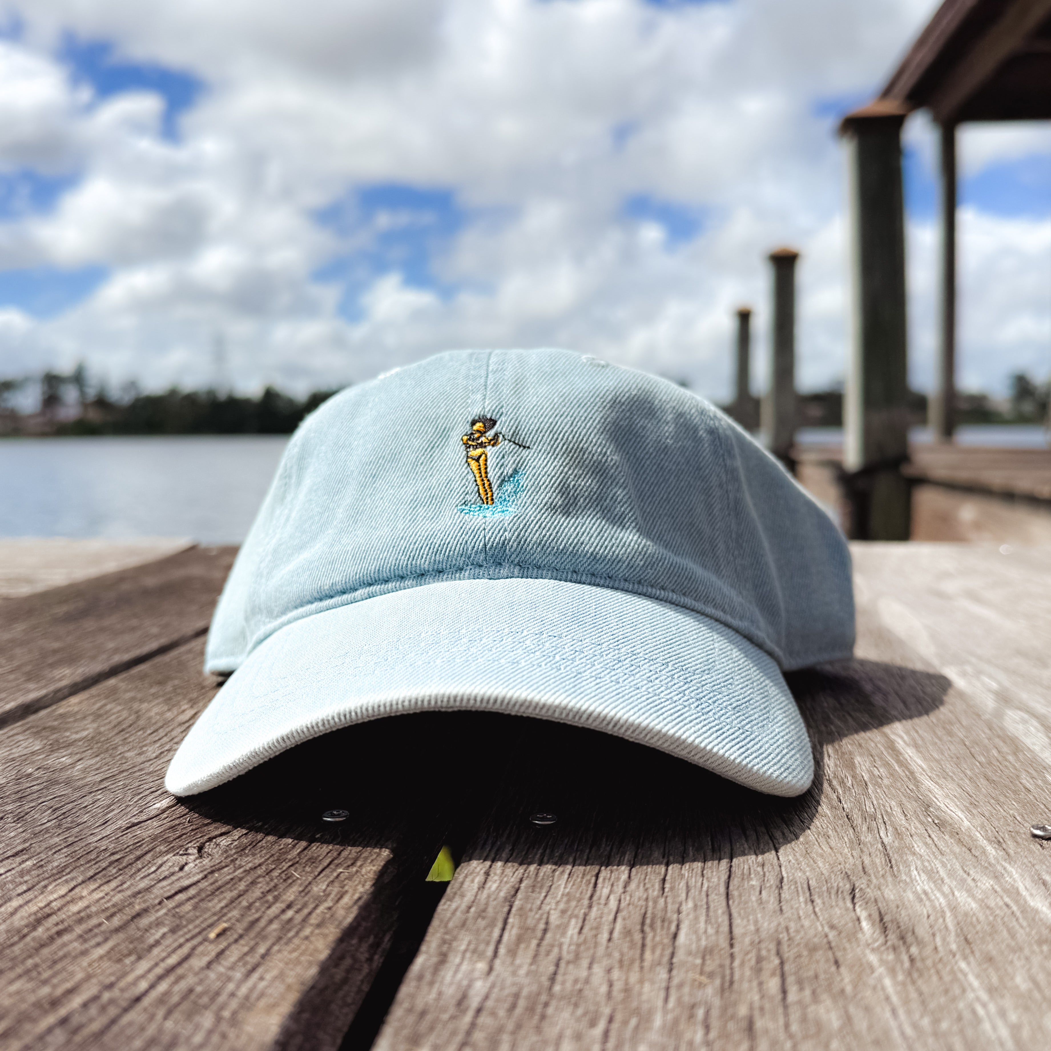Pink hat on a dock with a waterski girl design embroidered on the front of it.
