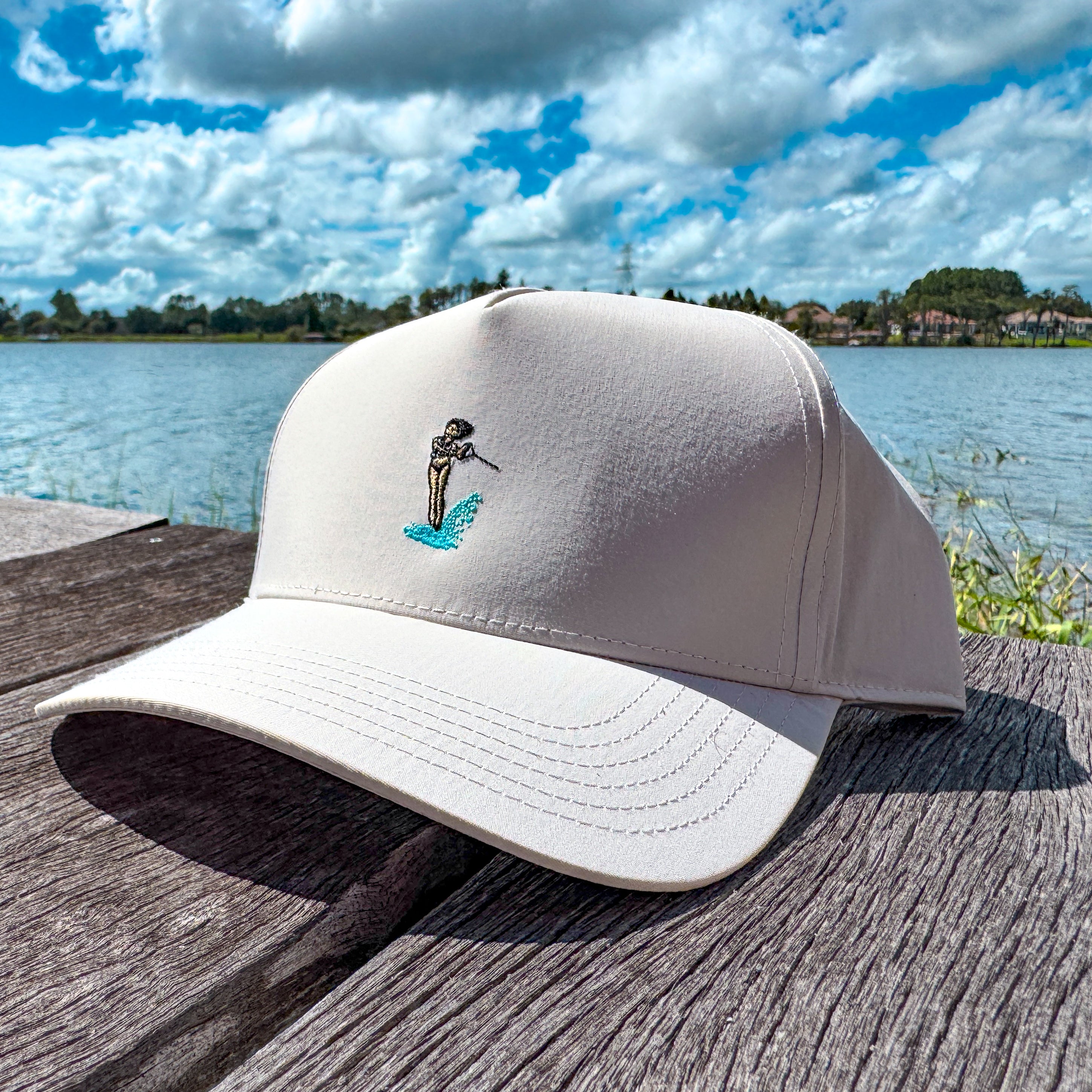 White cap with a waterskier embroidered on the front on a wooden dock by a lake