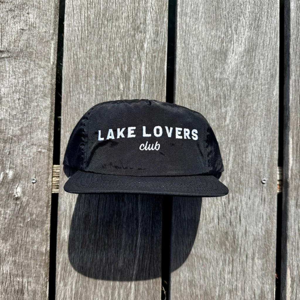Black cap with 'Lake Lovers Club' text on a wooden background