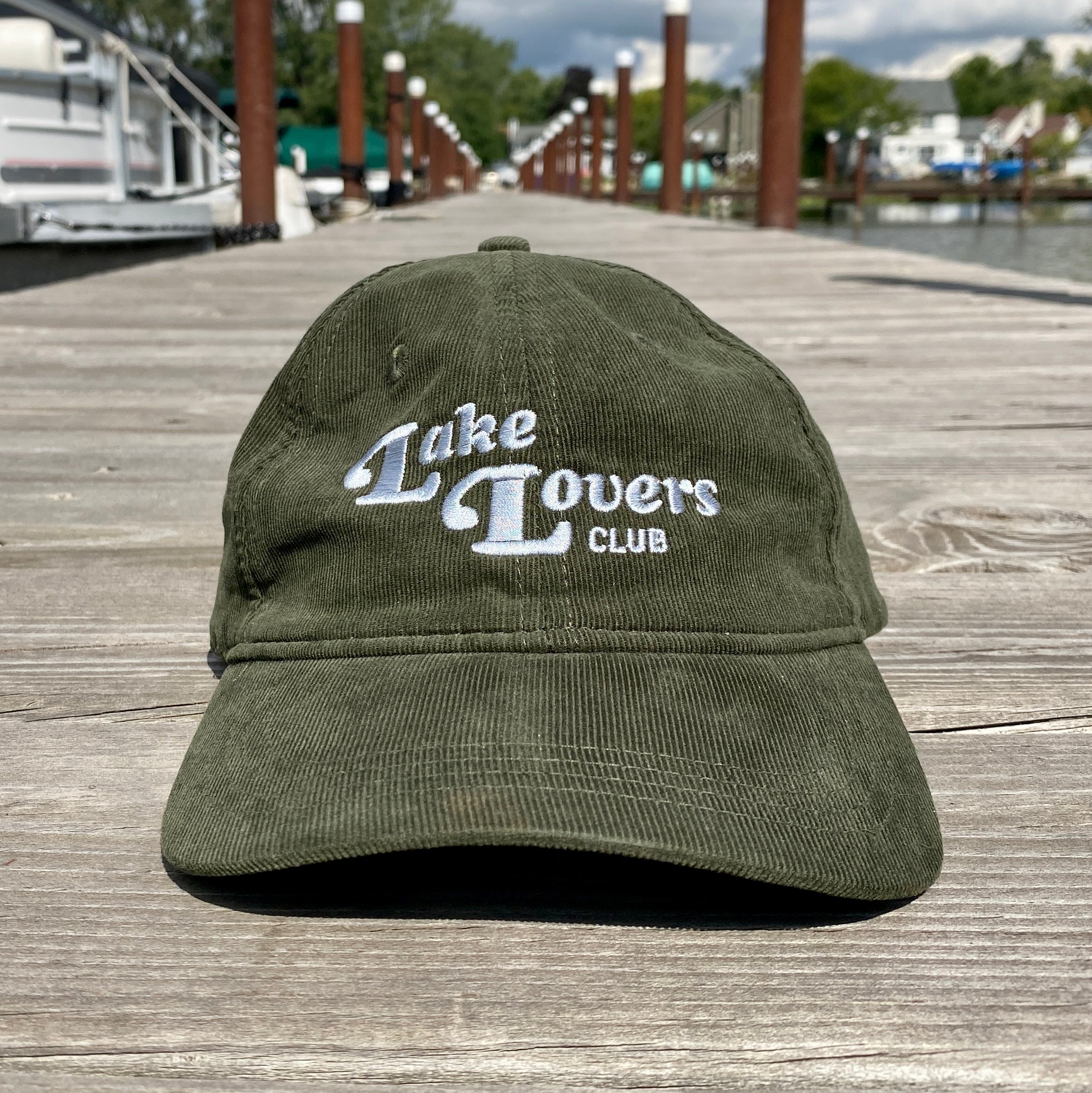 Green cap with 'Lake Lovers Club' text on a wooden dock.