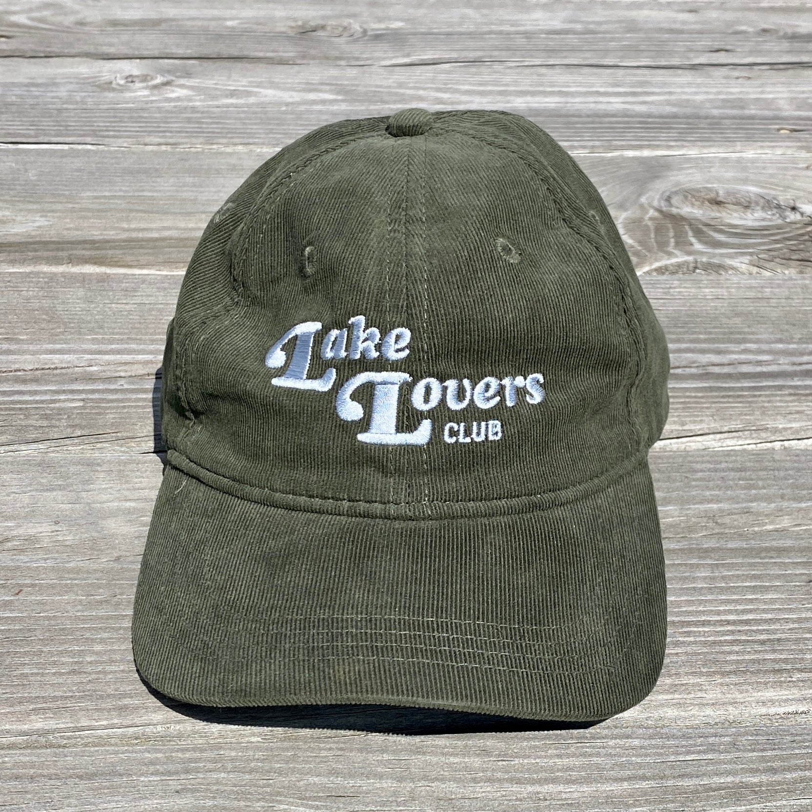 Green cap with 'Lake Lovers Club' text on a wooden surface