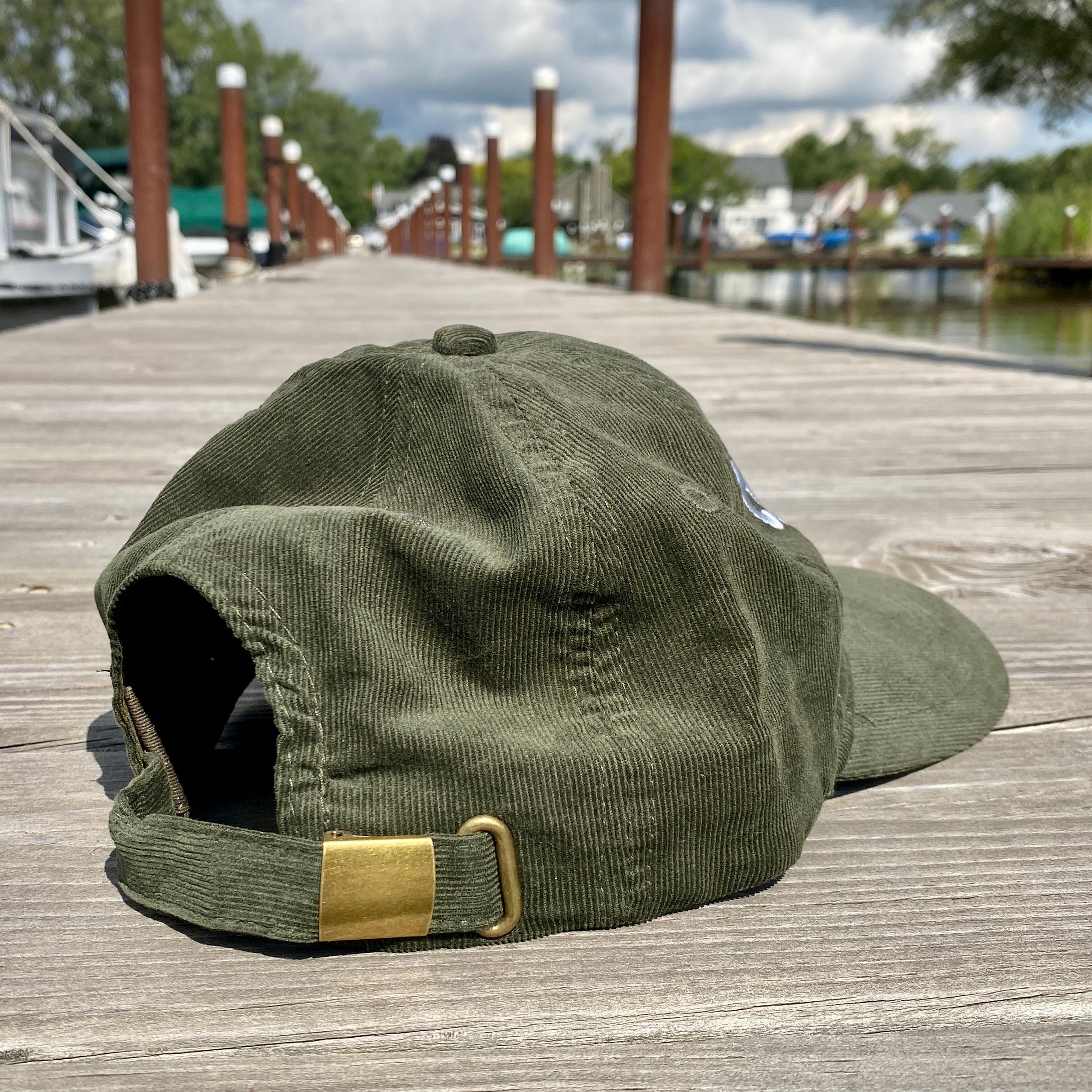 Green cap with a gold buckle on a wooden dock with water and boats in the background