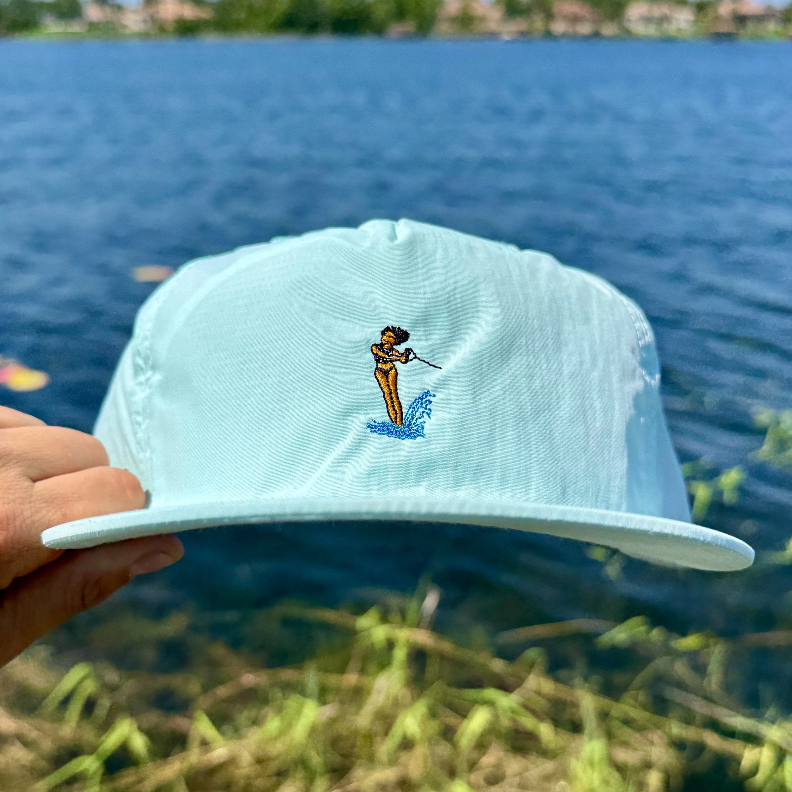 Light blue cap with a waterski design held over a body of water.