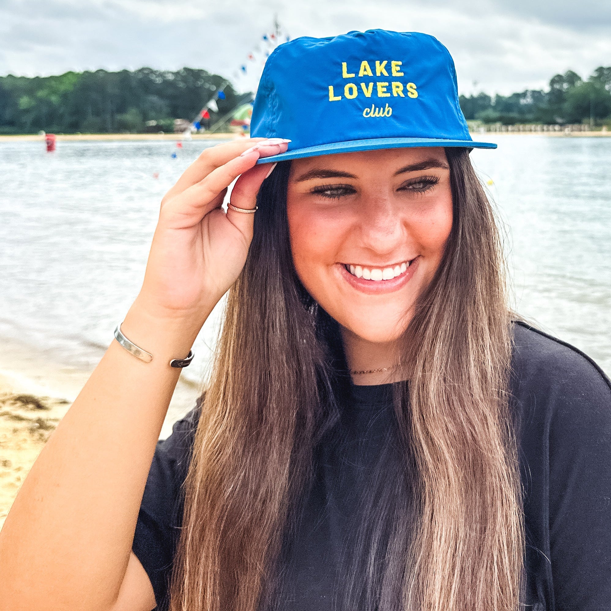 Woman wearing a blue cap with 'Lake Lovers Club' text by a lake.