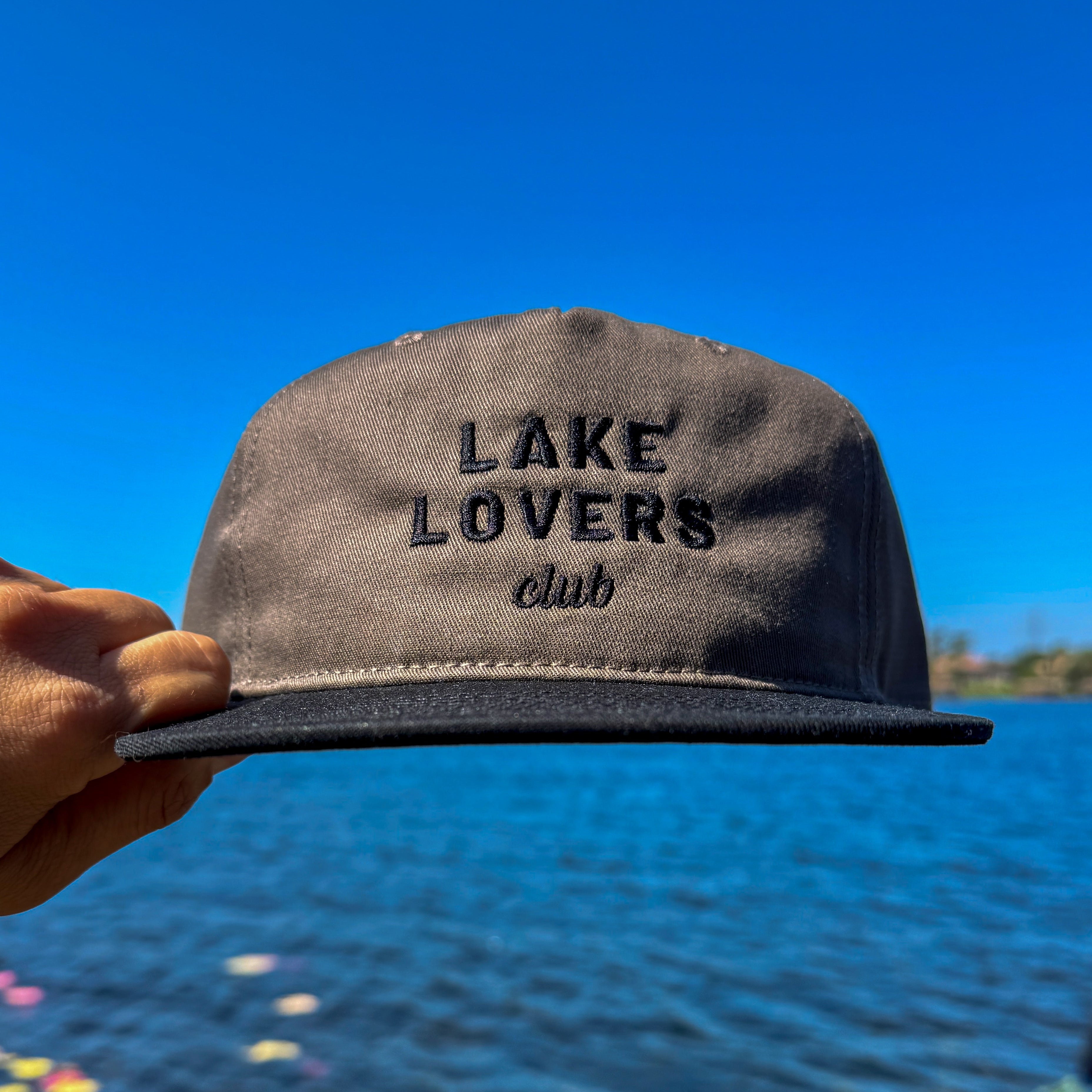 Cap with 'Lake Lovers Club' text held by a hand against a lake background
