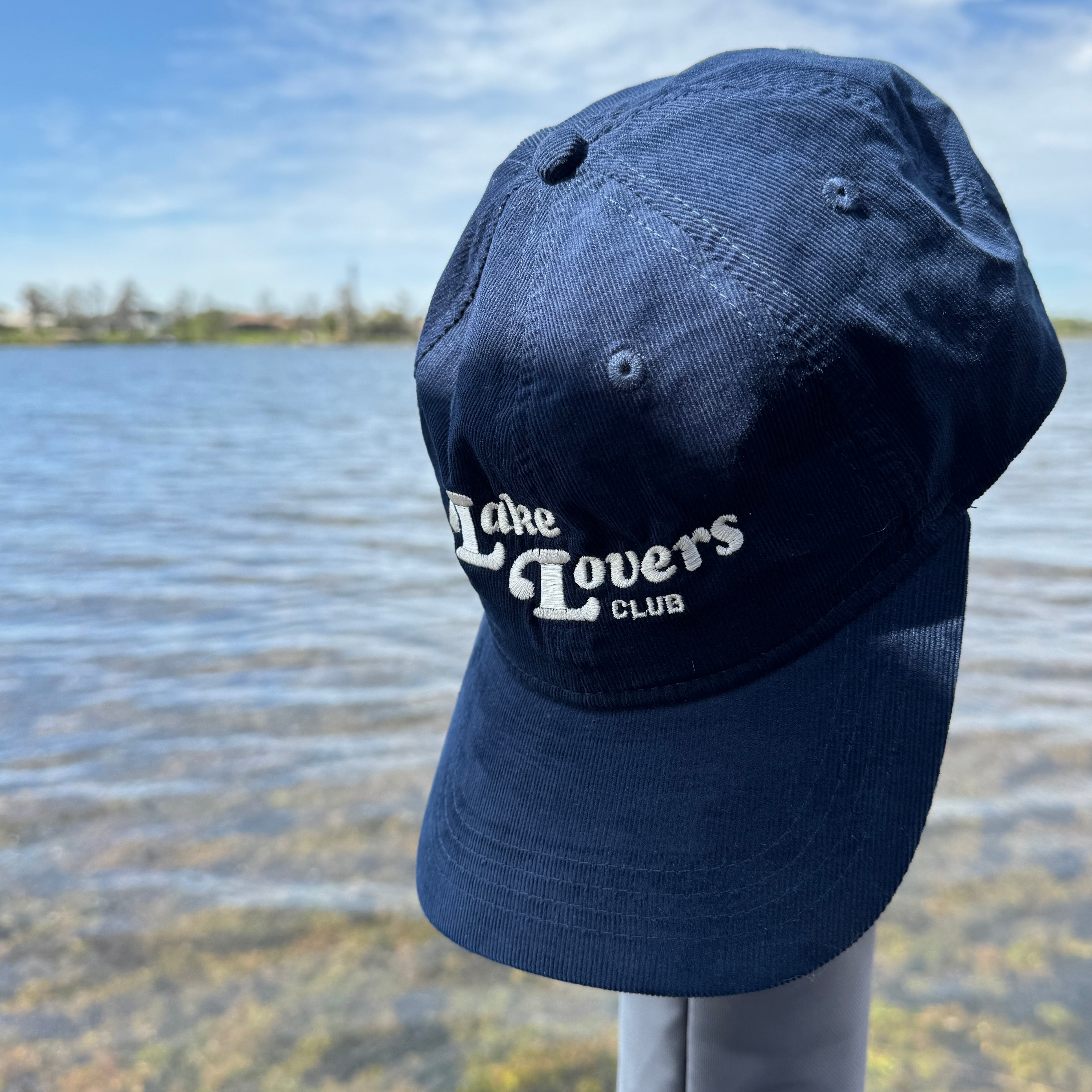 Navy blue cap with 'Lake Lovers Club' text against a lake background