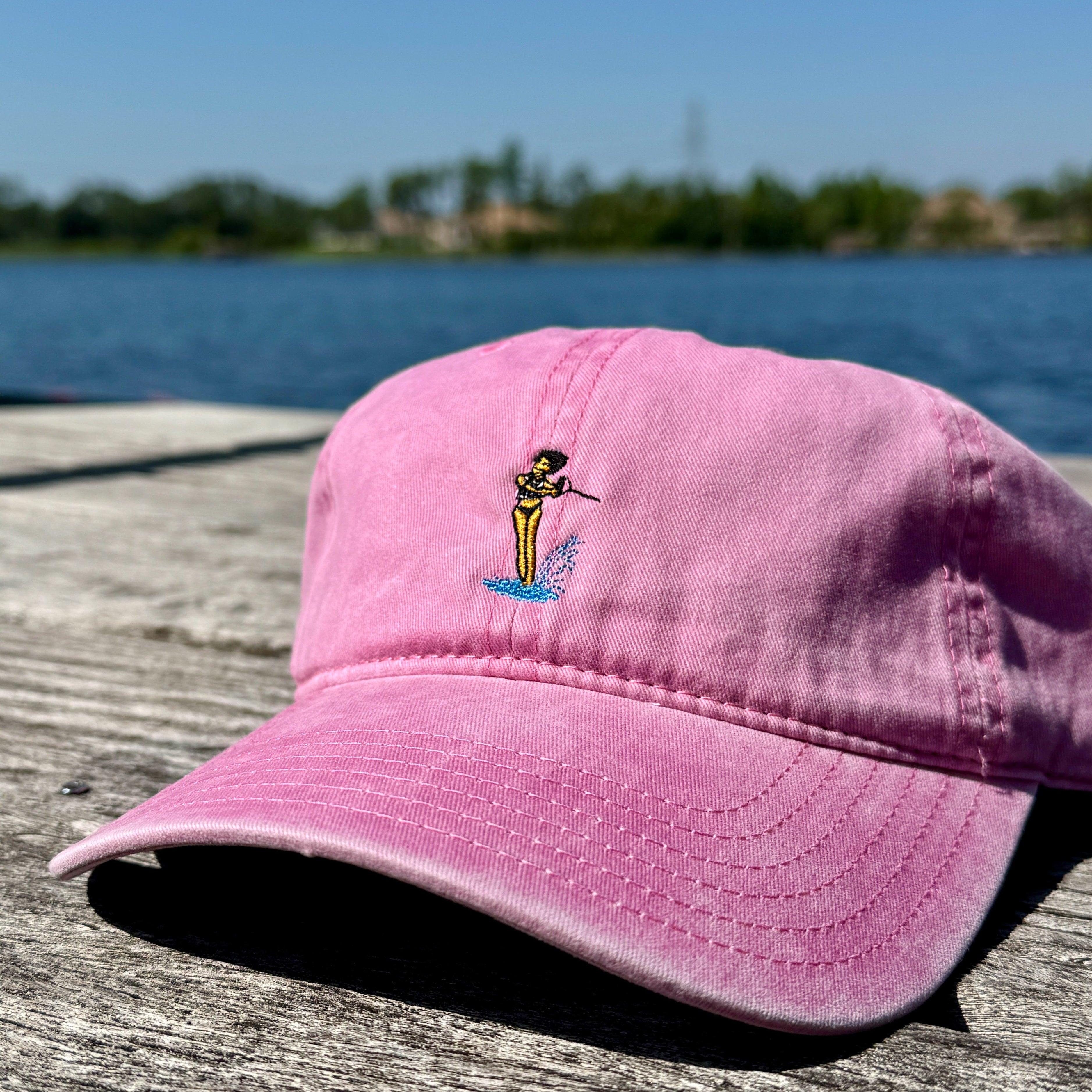 Pink hat on a dock with a waterski girl design embroidered on the front of it.