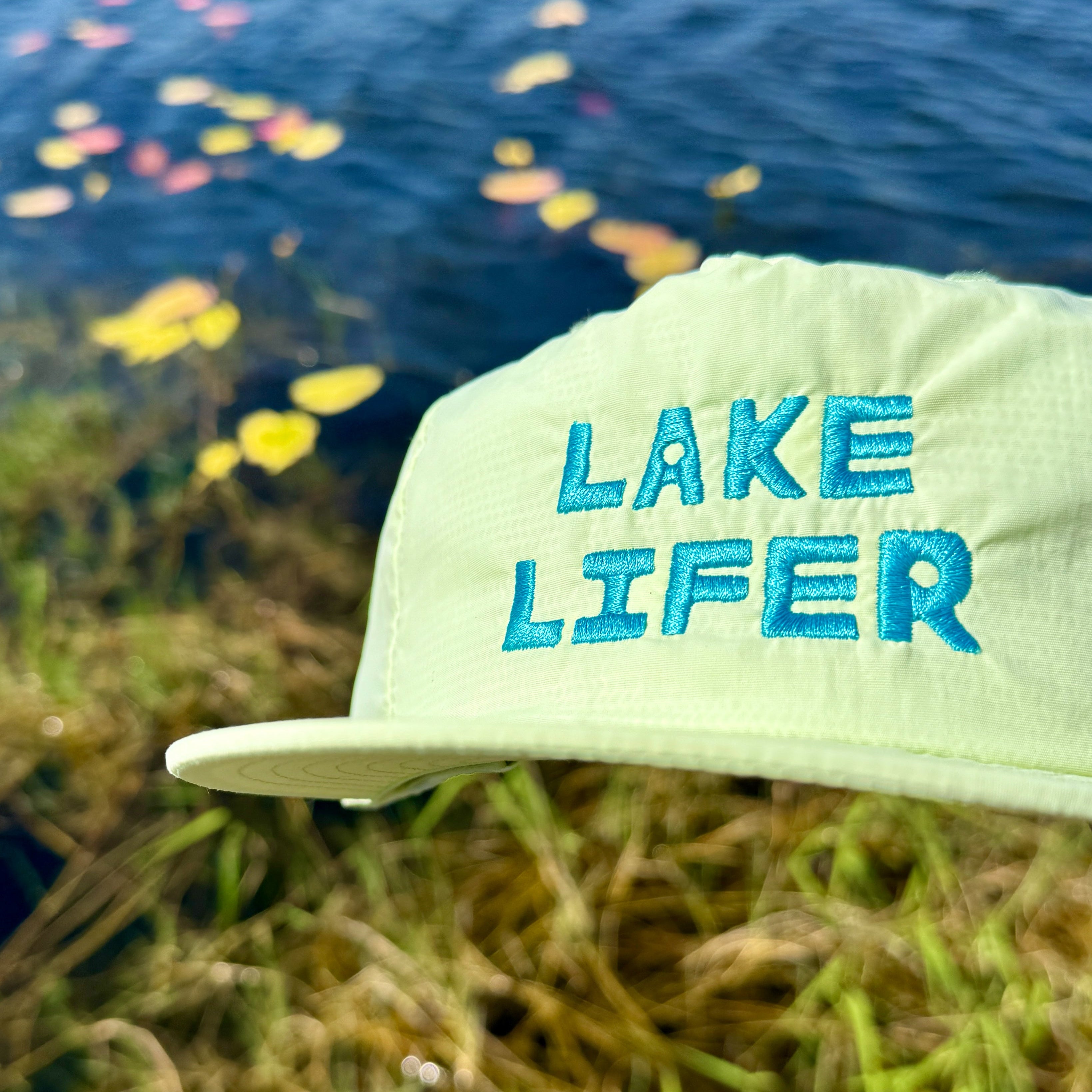 Cap with 'Lake Lifer' text in front of a lake with floating grass.