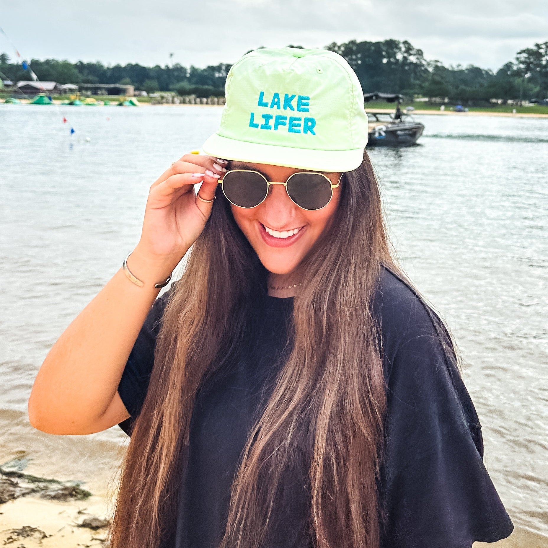 Person wearing a lime green 'Lake Lifer' cap by the water