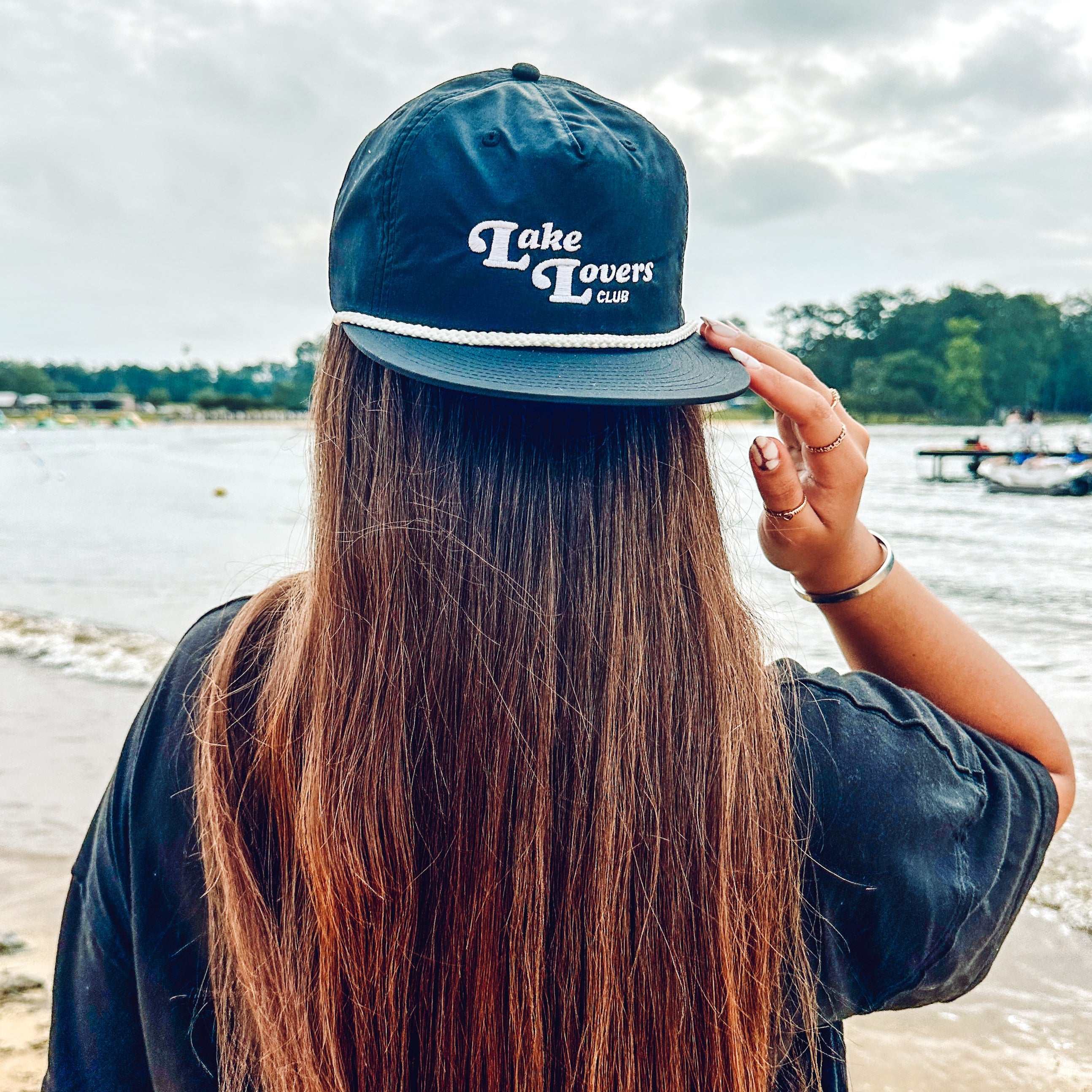 Woman wearing a backwards cap with 'Lake Lovers Club' text, facing a lake
