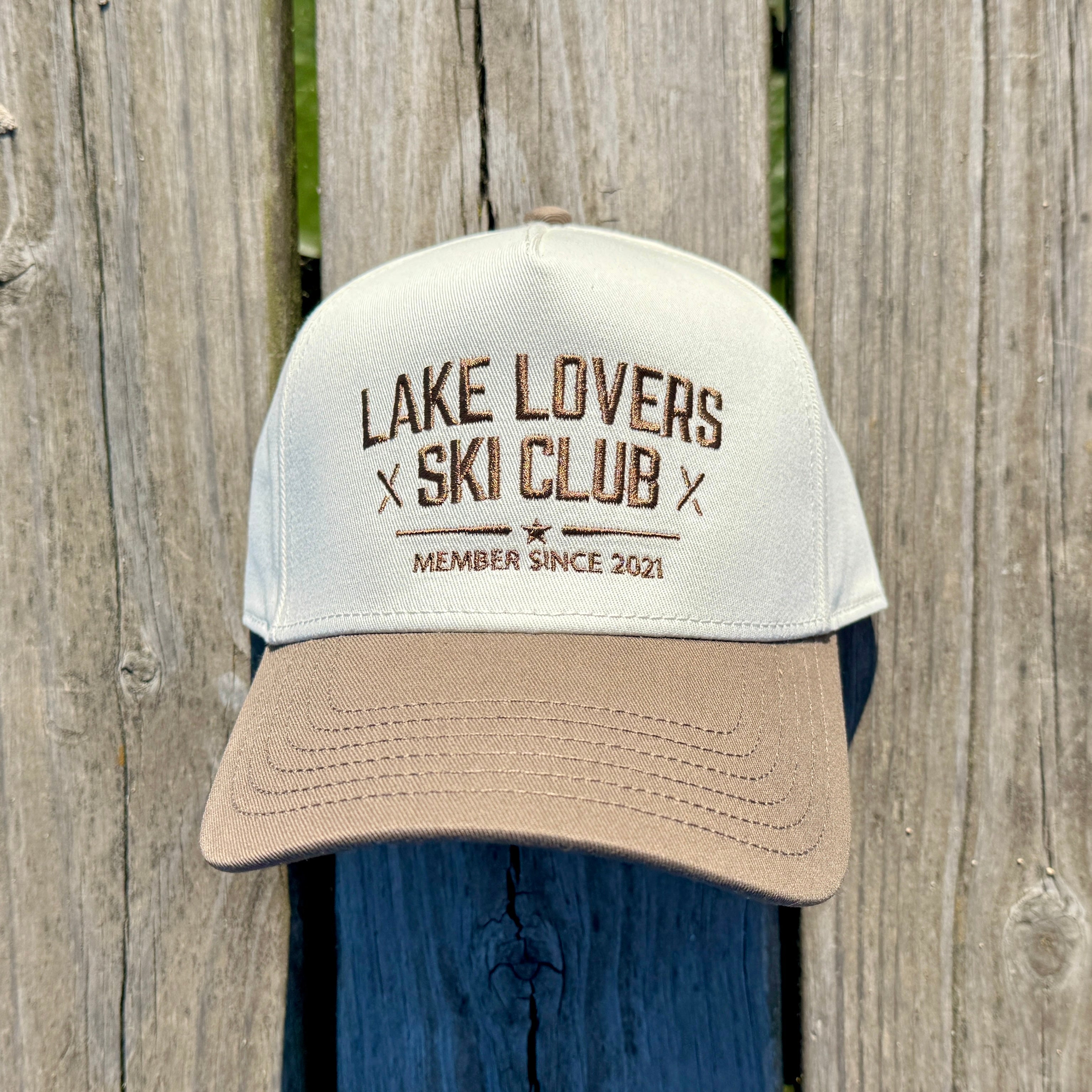 Beige hat on a dock with a brown brim and text on it in brown that says Lake Lovers Ski Club.