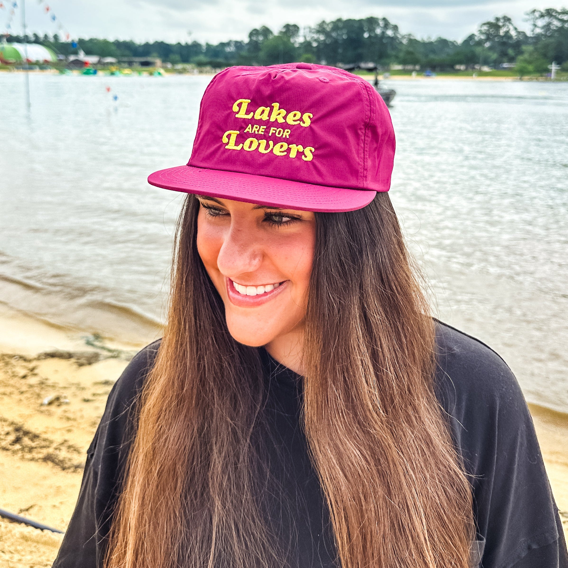 Person wearing a maroon cap with 'Lakes are for Lovers' text by a lake.