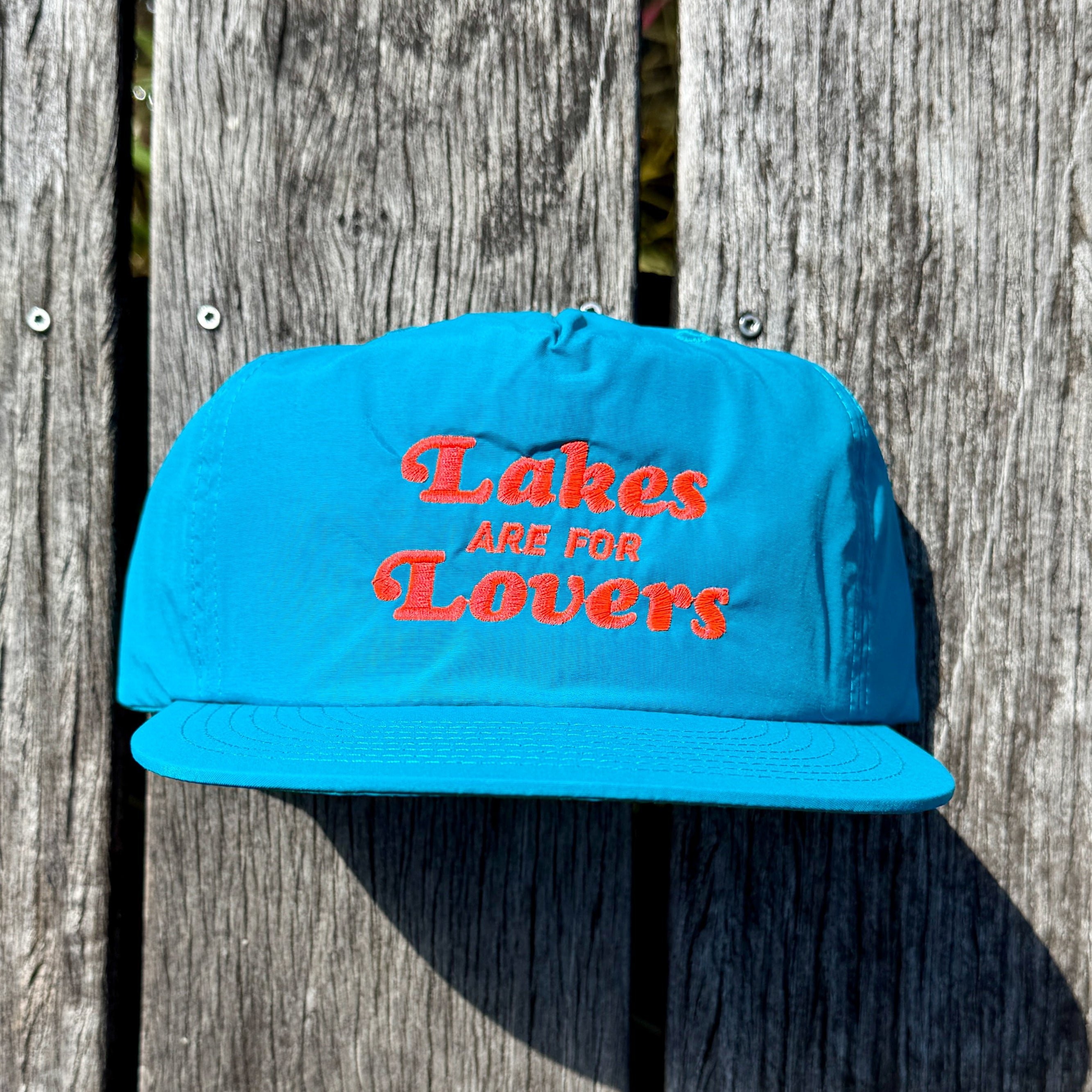 Teal hat that reads 'Lakes are for Lovers," lying on a dock.