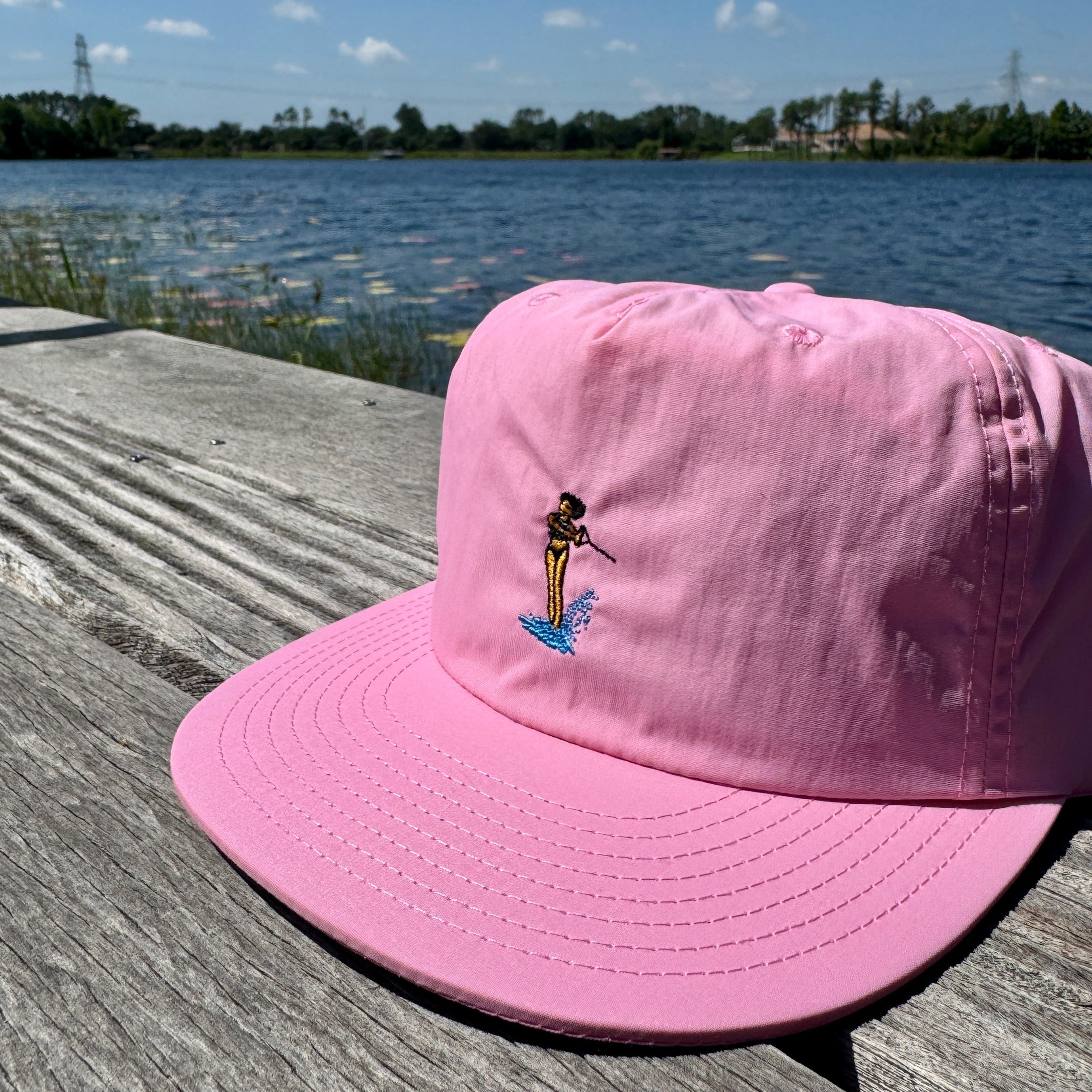 Pink cap with a waterski design on a wooden dock by a lake